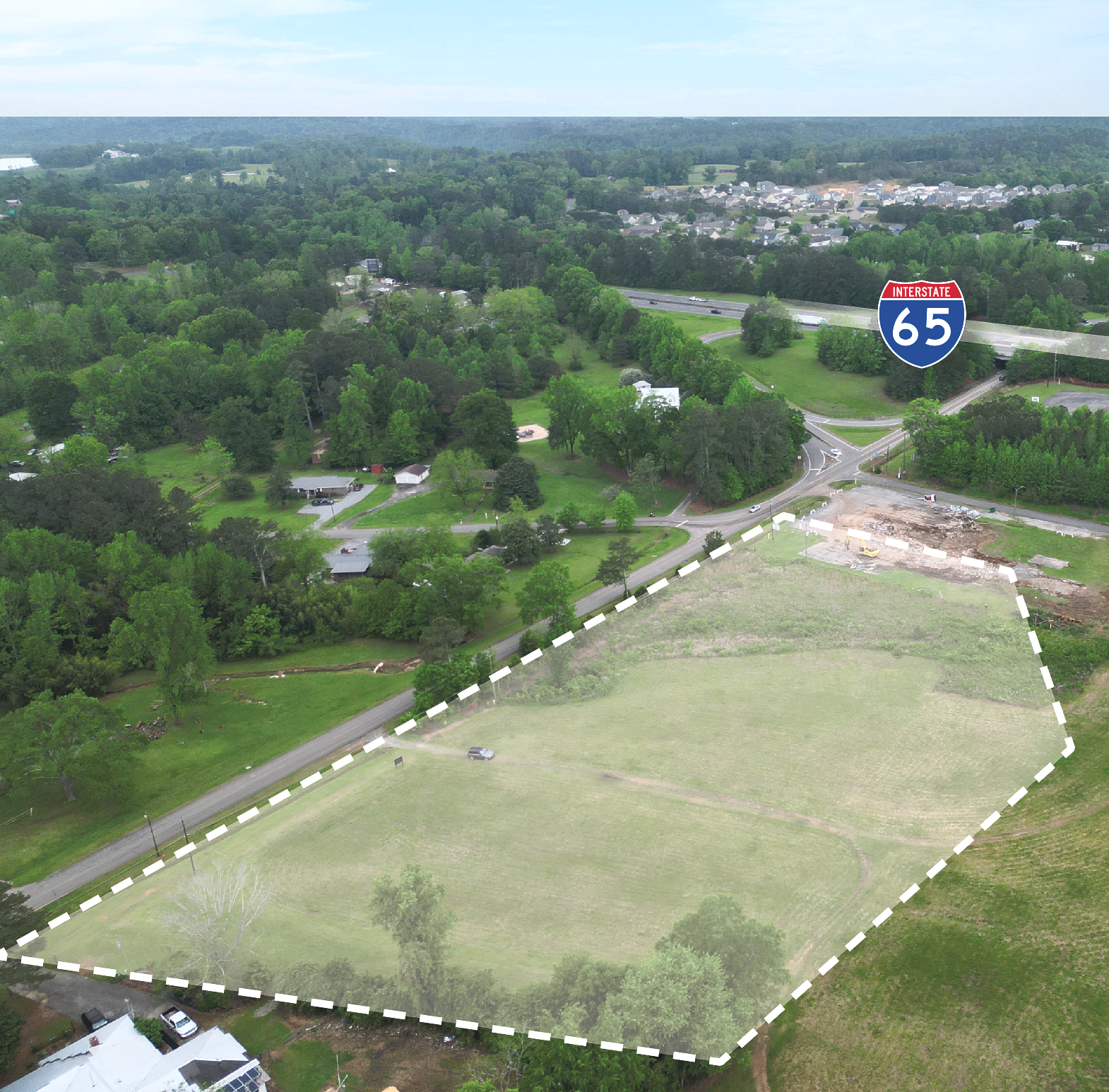 Aerial view of a grassy lot available on-market for development in Warrior AL, with a road and trees in the background.