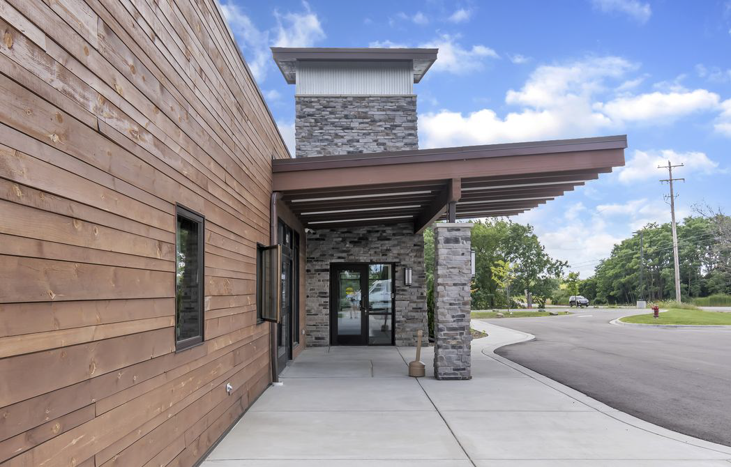 Exterior of a modern building with brown wood siding and a stone entrance under a wooden canopy.