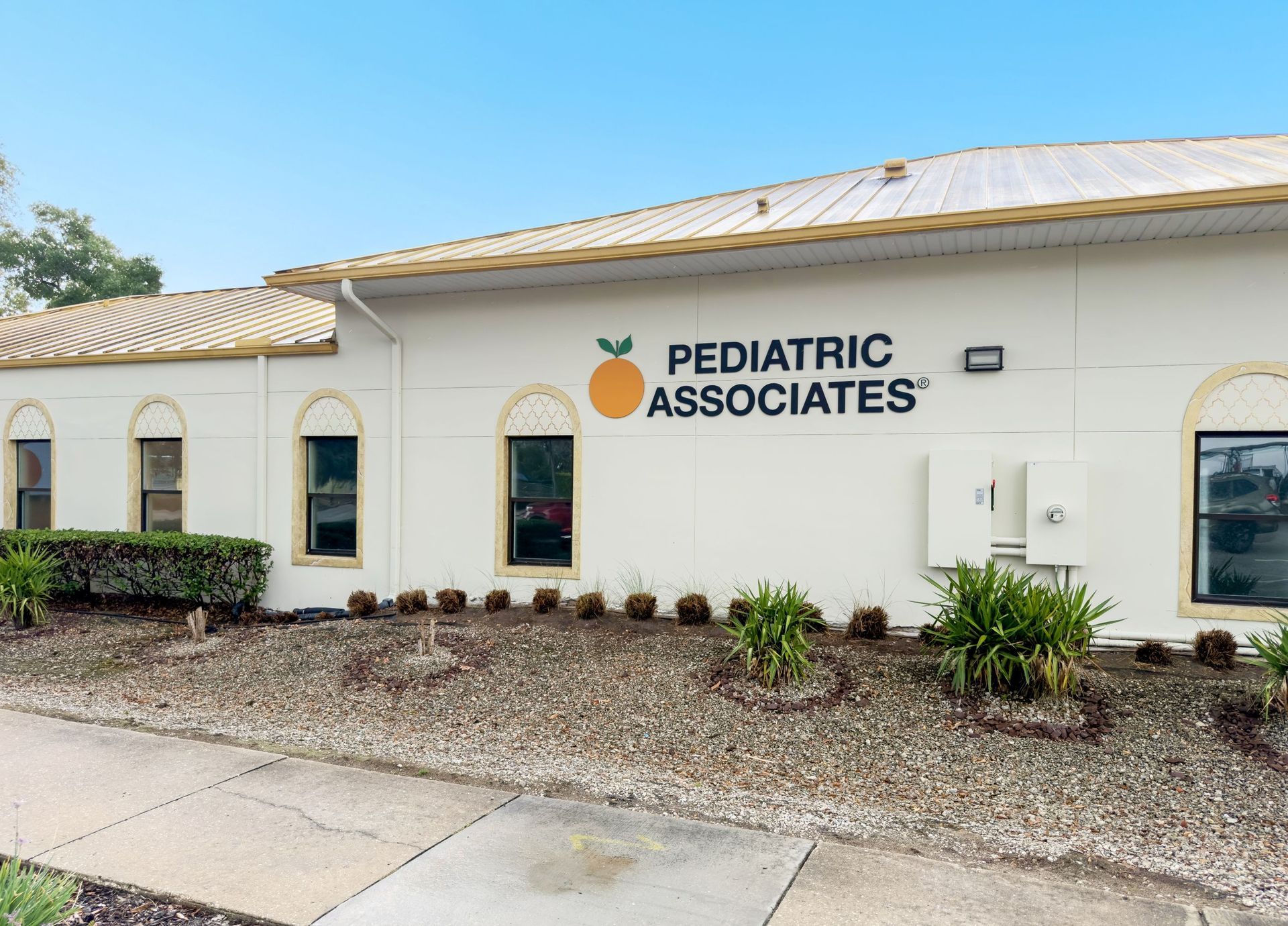 Pediatric Associates clinic exterior in Winter Springs, FL with white stucco walls, arched windows, and orange logo sign