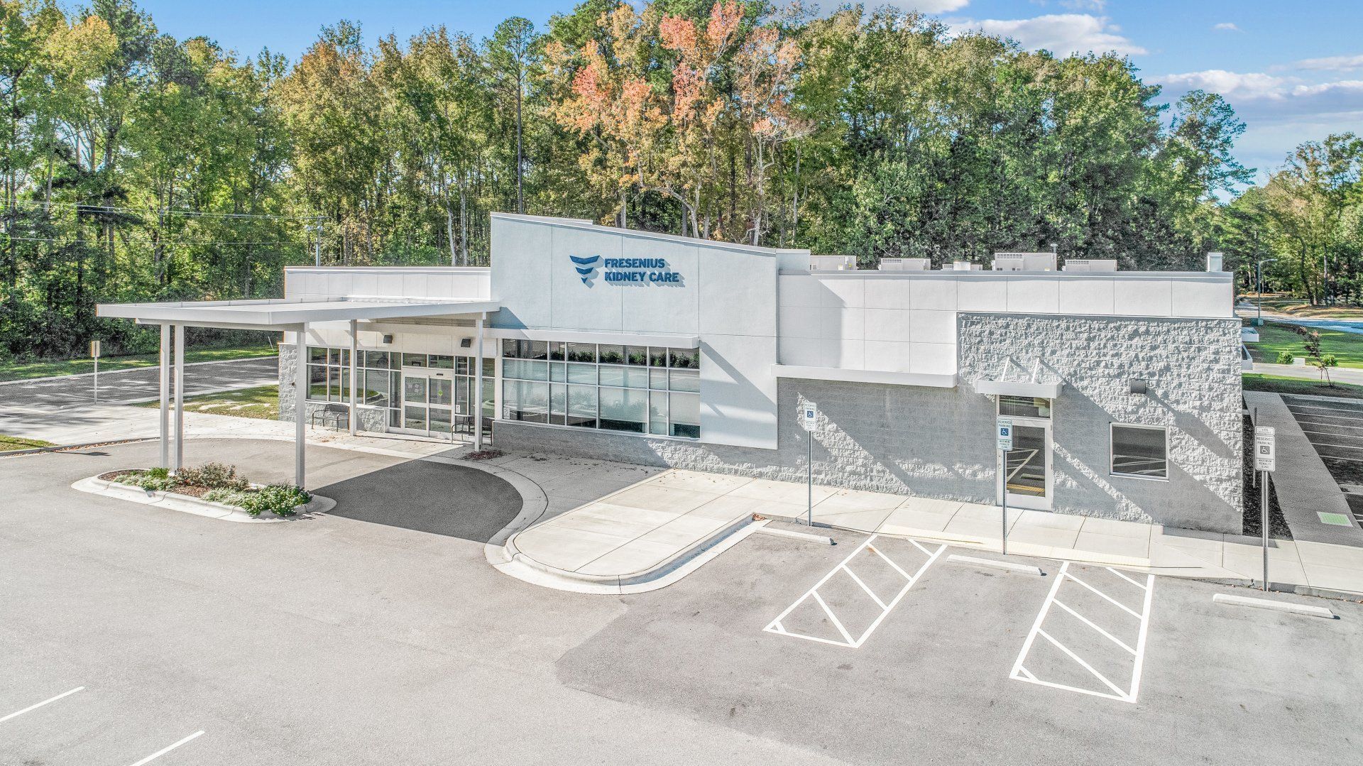 A large white fresenius dialysis building with a parking lot in front of it.