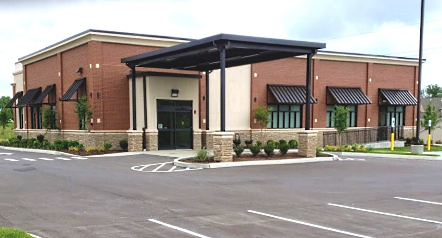 A large brick dialysis building with a parking lot in front of it