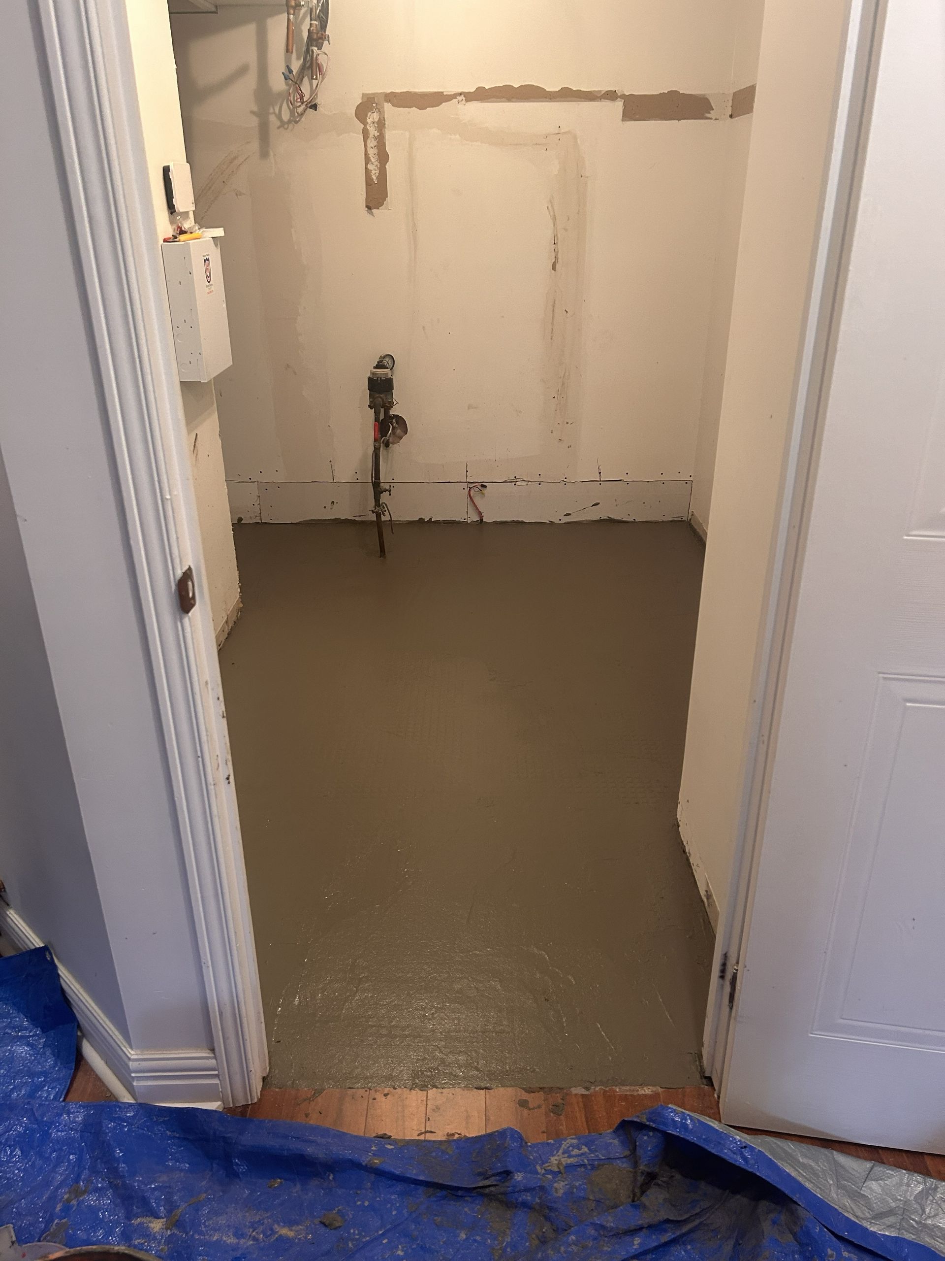 Un sol en béton gris lisse, fraîchement coulé, dans une petite buanderie aux murs bruts et avec un tuyau apparent.