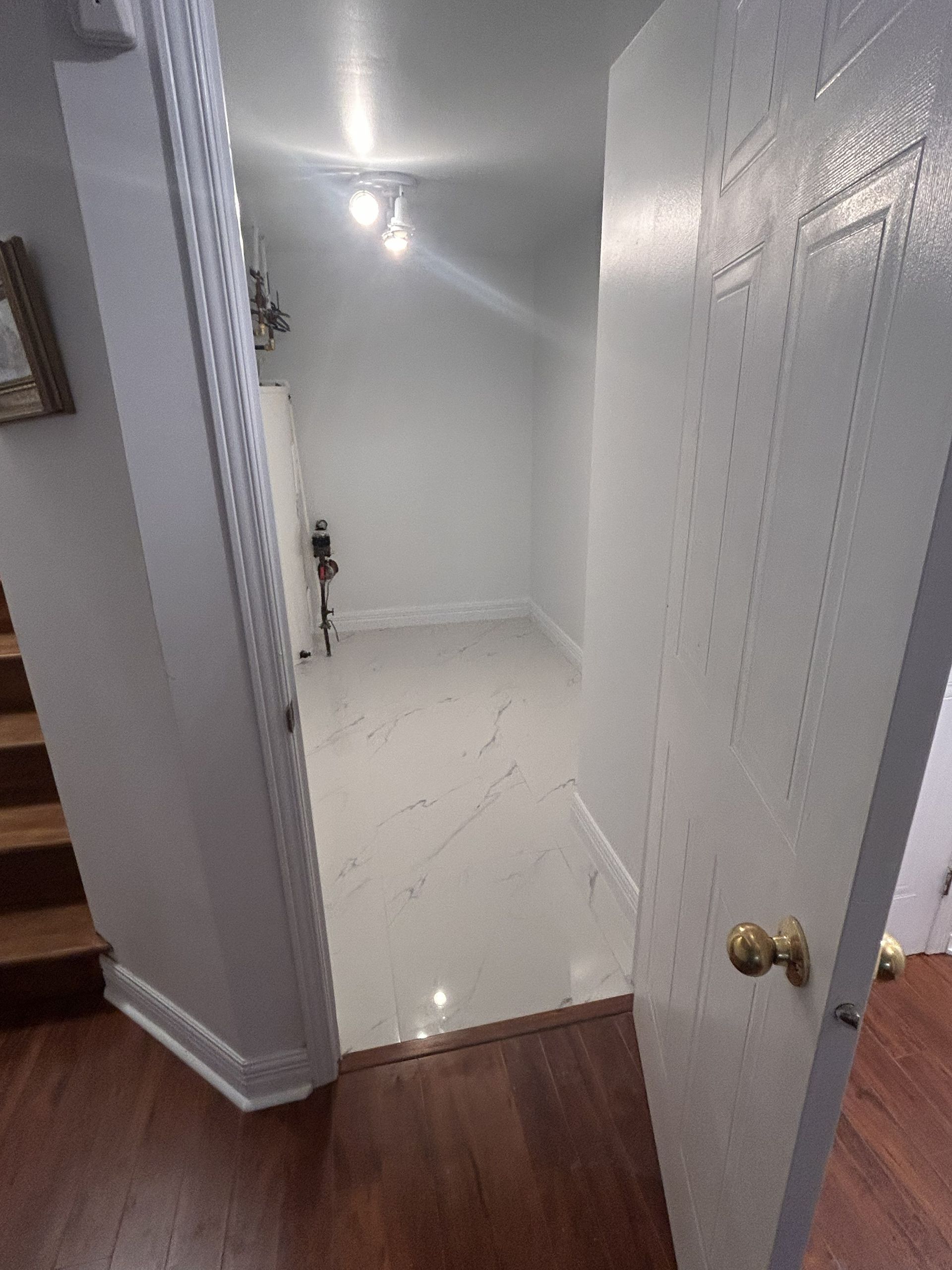 Une porte ouverte donnant sur une petite pièce au sol carrelé de carreaux clairs à motifs marbrés et aux murs blancs.