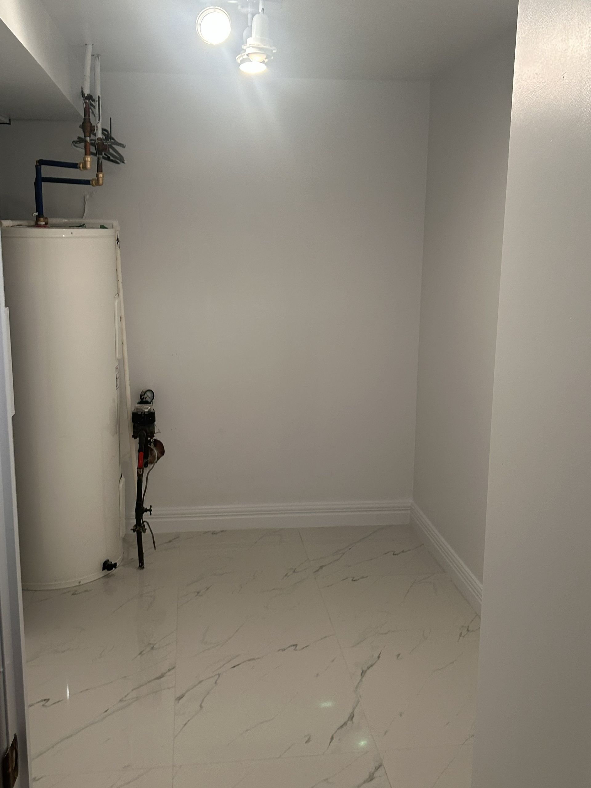 Buanderie avec sol en marbre blanc à motifs, murs gris unis et un grand chauffe-eau blanc dans un coin.