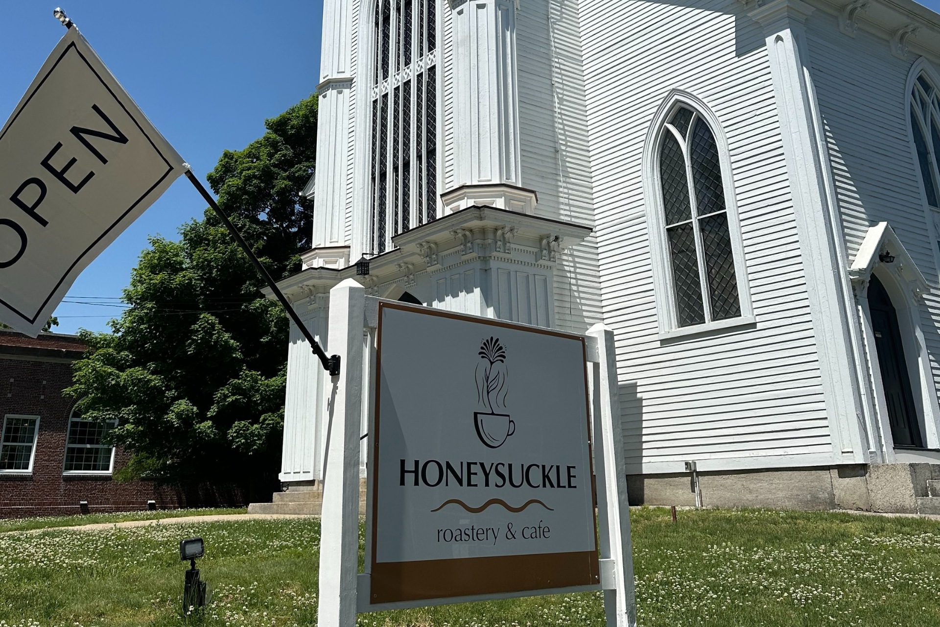 A white building with a sign in front of it that says honeysuckle roastery and cafe