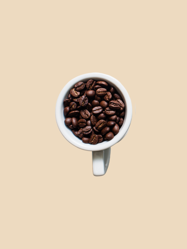 A cup filled with coffee beans on a beige background.