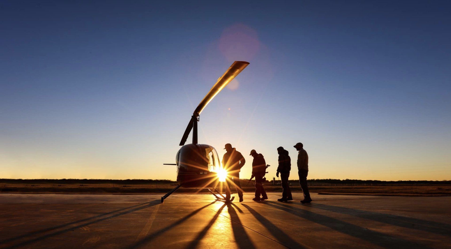 a group of people are standing in front of a helicopter at sunset.