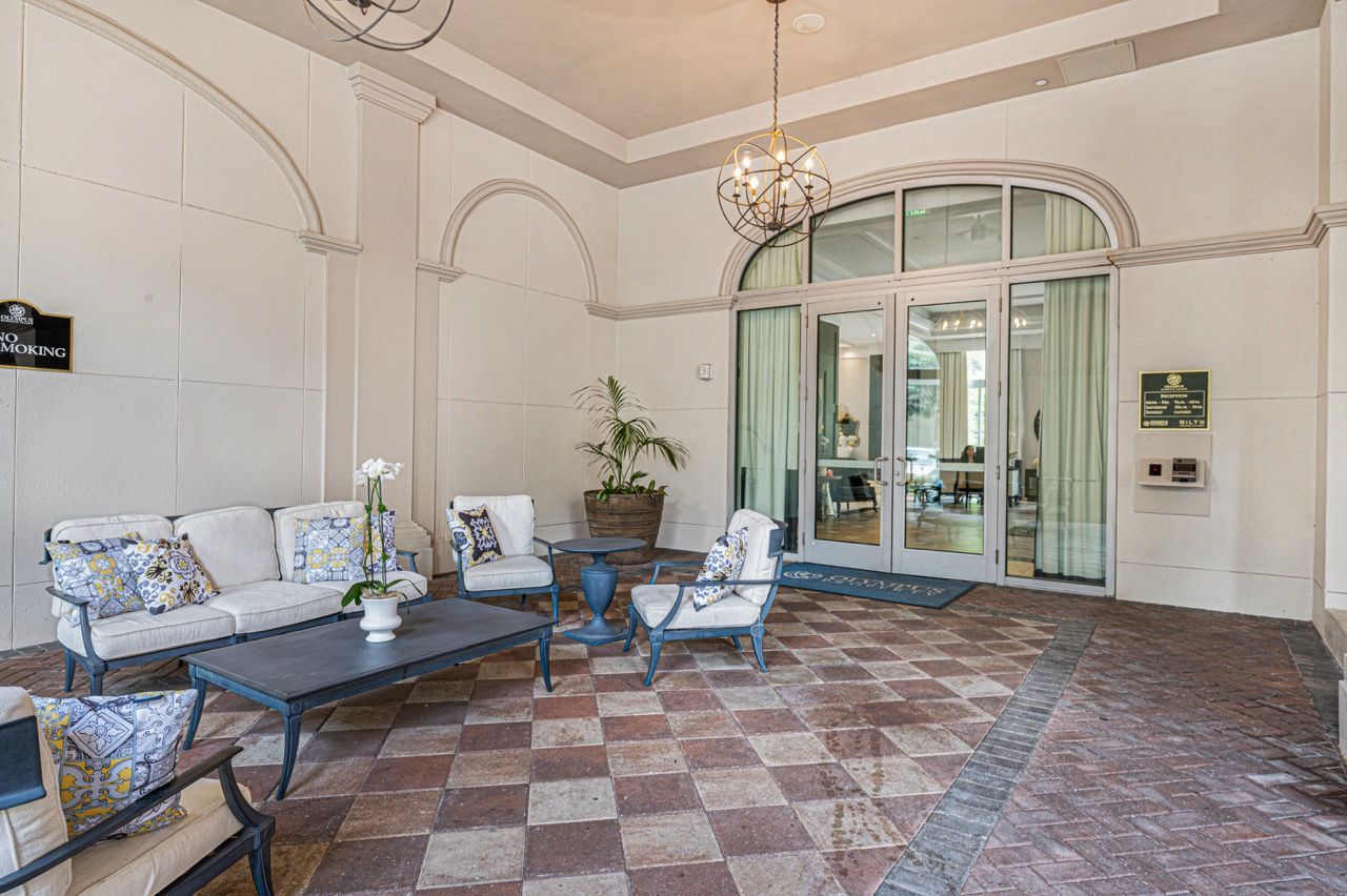 Covered building entrance with white walls, arched alcoves, and outdoor seating near glass doors at Olympus Harbour Island, offering pet-friendly apartments in downtown Tampa.