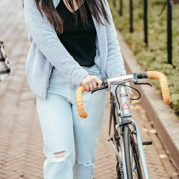 Person walking with a bicycle, wearing light blue jeans, black top, and gray sweater, holding the handlebar.
