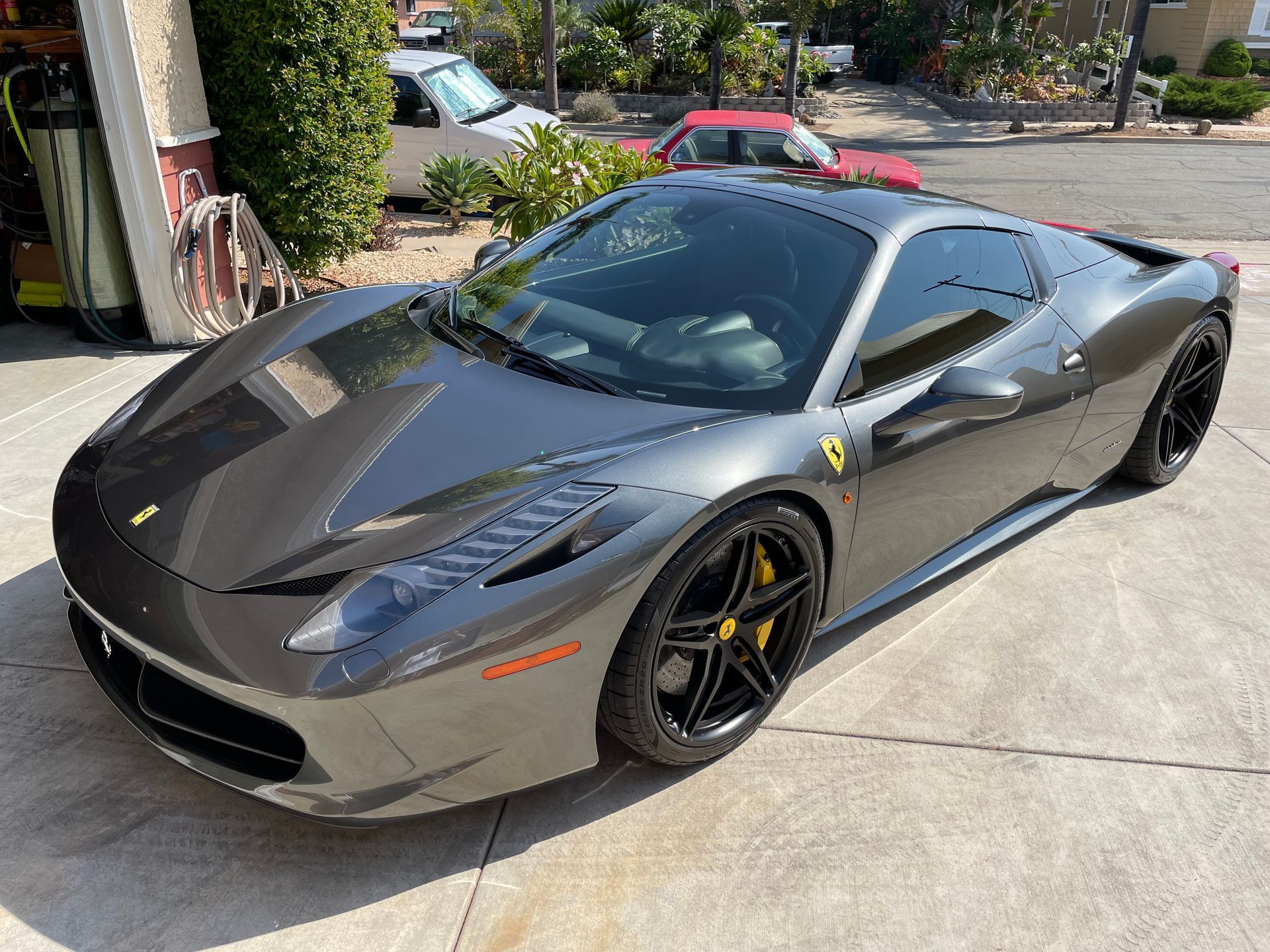 Gray Ferrari sports car parked on a driveway, black wheels with yellow brake calipers.