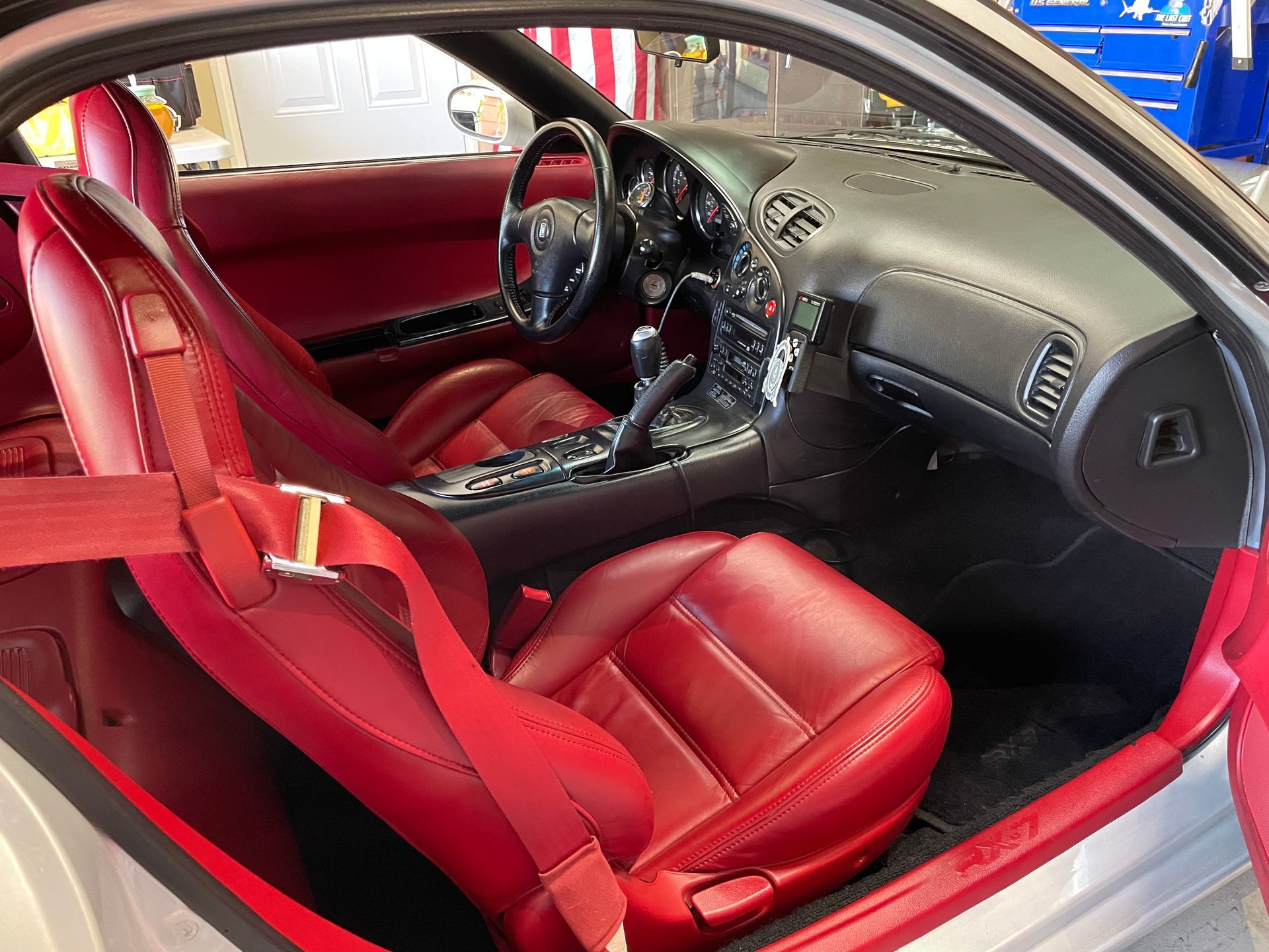 Red leather car interior with seat belts, dashboard, steering wheel.