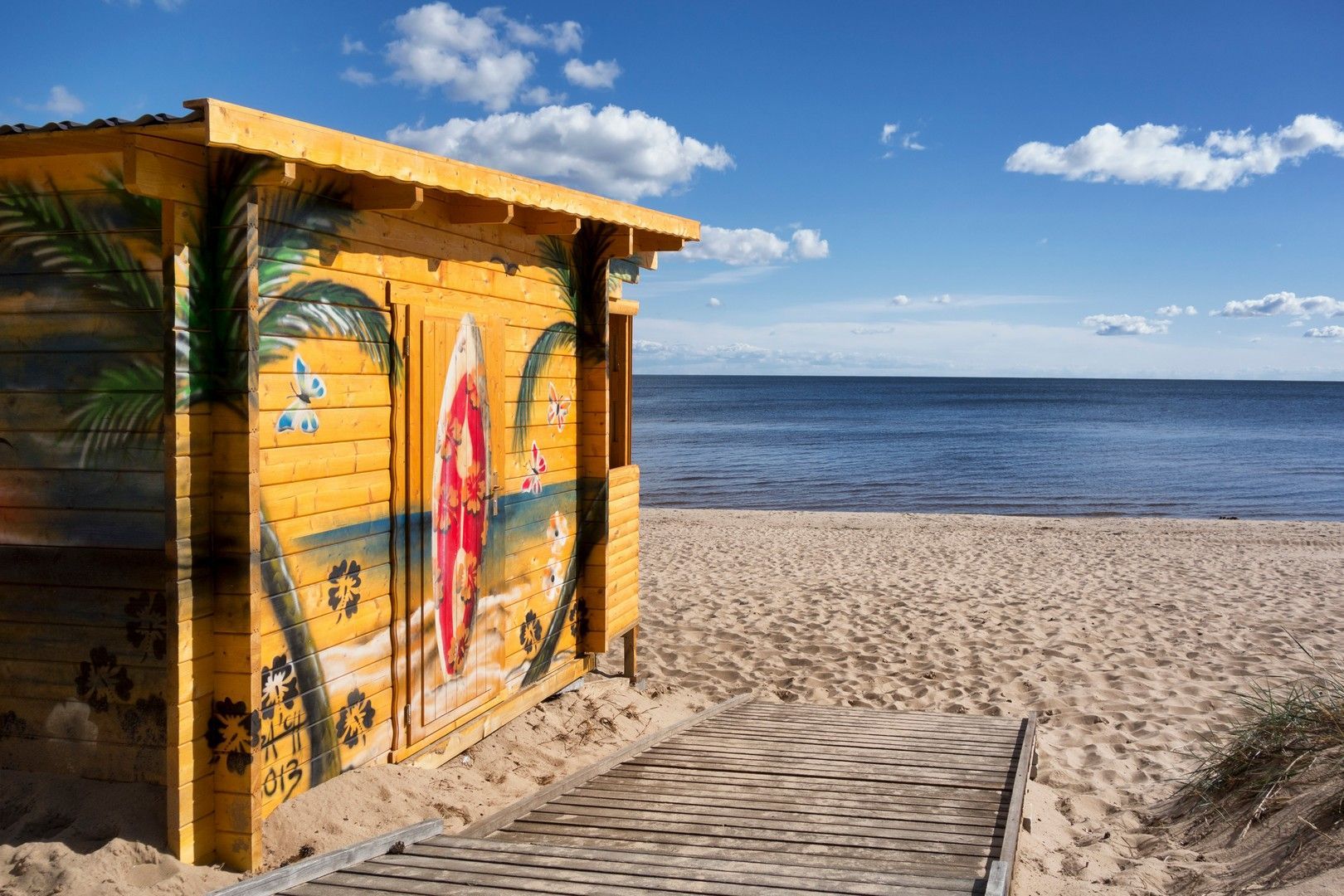 Una baracca di legno sulla spiaggia con sopra dipinto una tavola da surf.