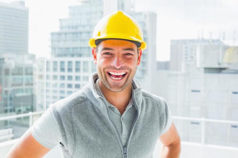 A man wearing a hard hat and a vest is smiling.