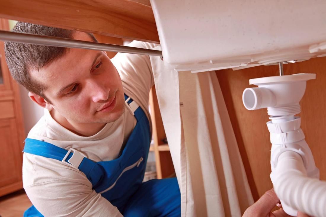 A man in blue overalls is fixing a sink drain