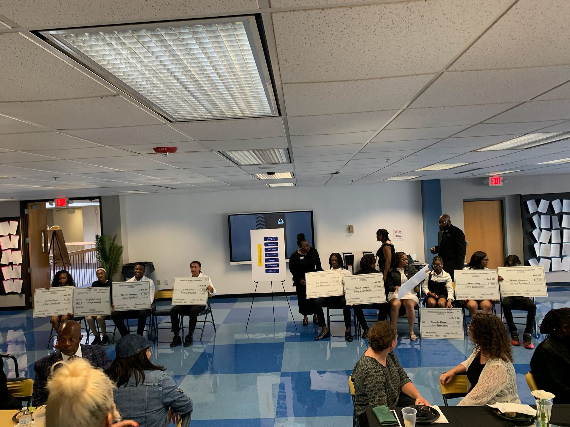 A group of people are sitting at tables in a large room holding signs.