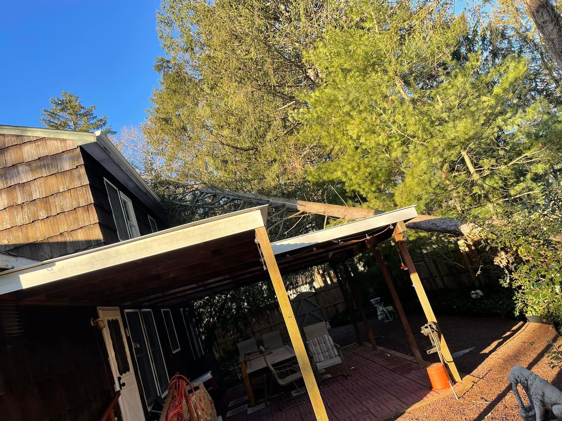 A porch with a brown roof, deck, and white pillars, with trees and a blue sky in the background.