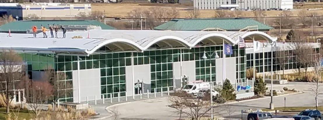 A modern airport terminal with a distinctive wavy, barrel-vaulted metal roof and large floor-to-ceiling glass windows.