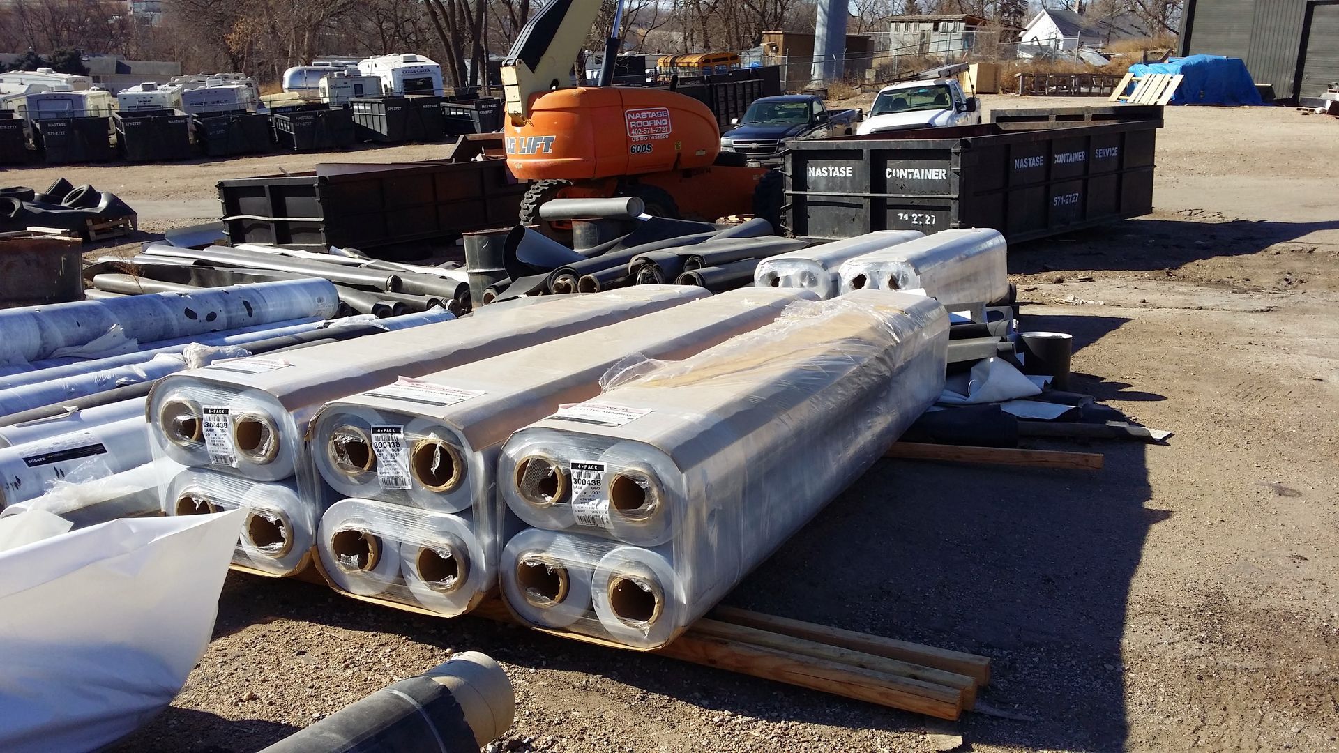 Stacked bundles of silver cylindrical components on wooden pallets in an industrial outdoor lot.