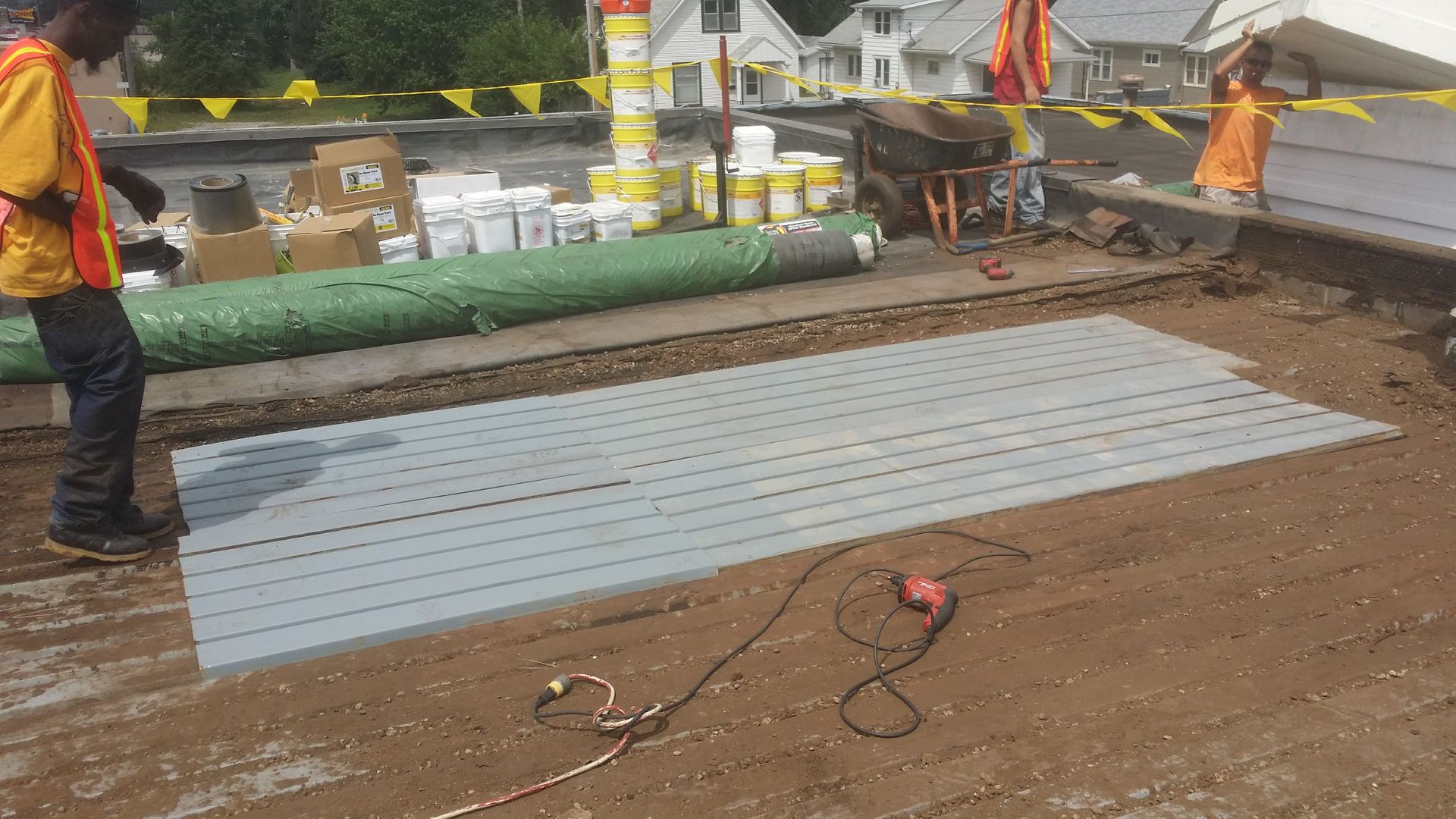 Two workers in high-visibility vests work on a flat rooftop, installing a large, rectangular gray panel.