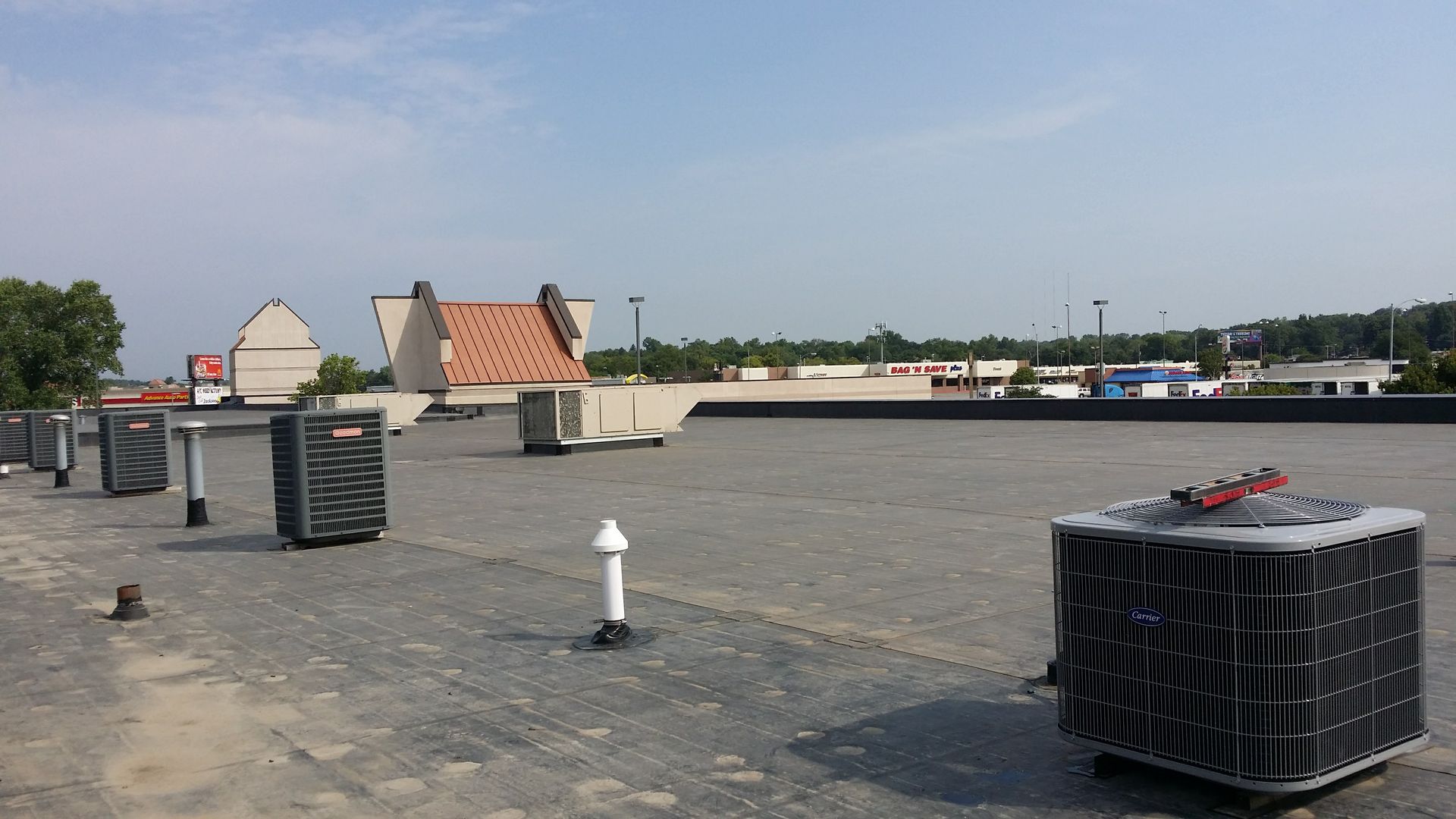 A rooftop with several HVAC units, including one in the foreground, under a clear, bright sky.