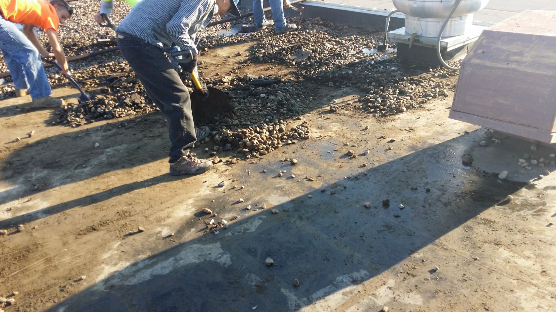 Workers use shovels to clear gravel from a flat rooftop.