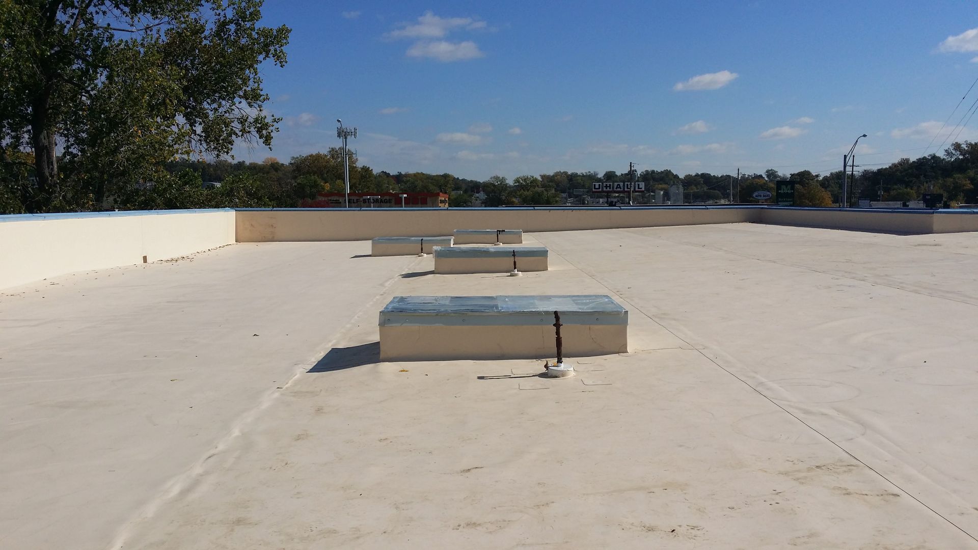 A flat, beige rooftop under a clear blue sky, featuring several low, rectangular skylights and a parapet wall.