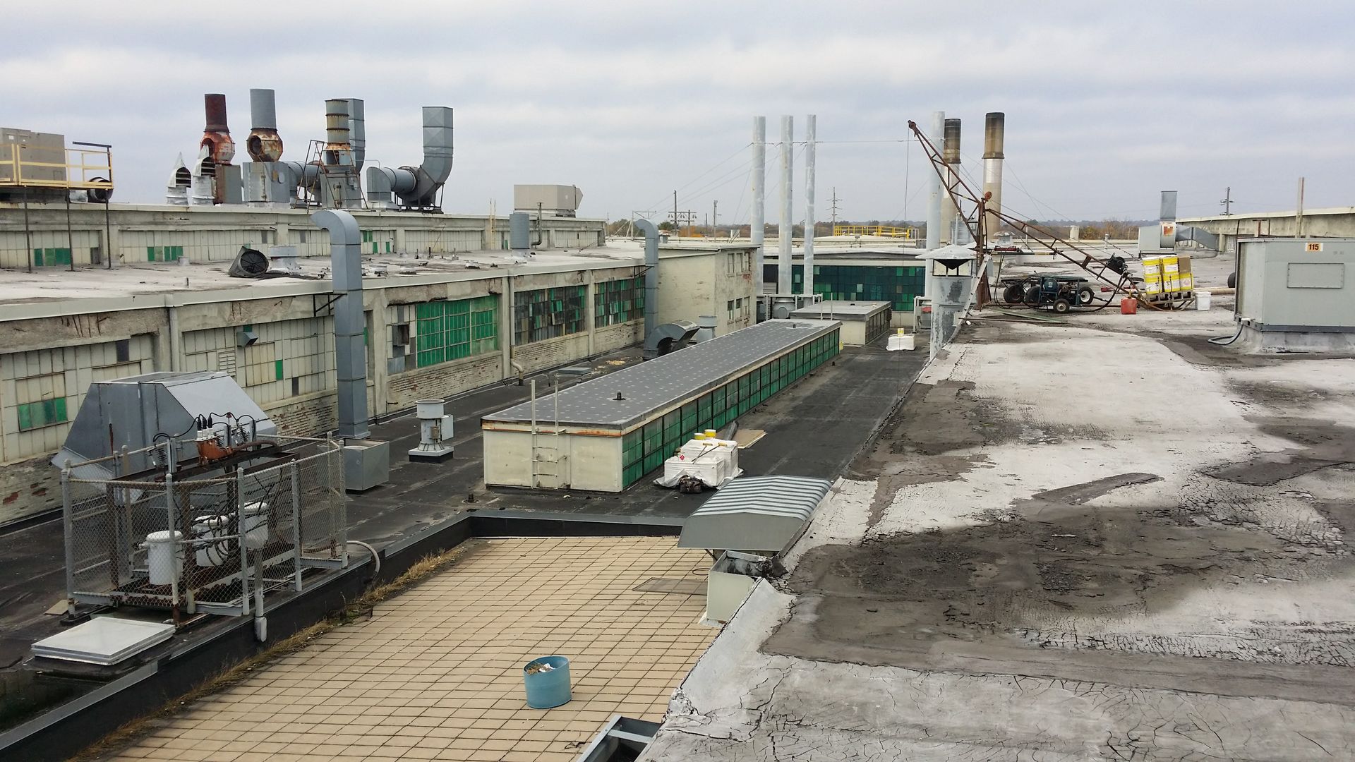 A rooftop view of a large, industrial facility featuring various ventilation pipes, a long structure, and worn surfaces.