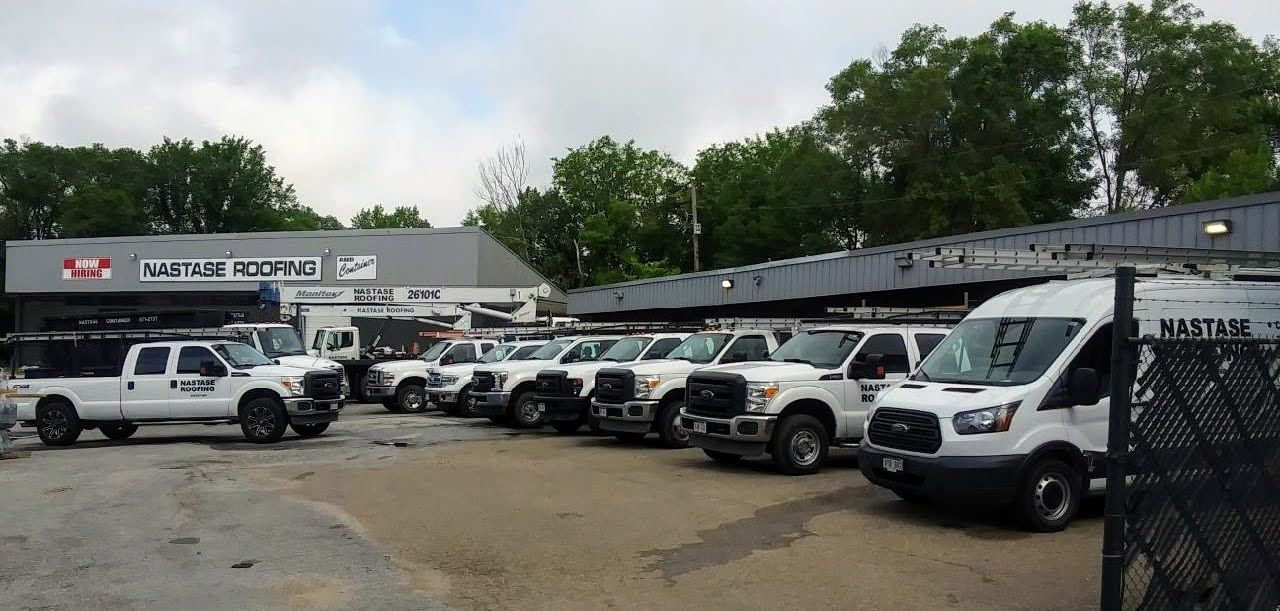 A row of white service vans and trucks parked in a lot in front of a building with a 