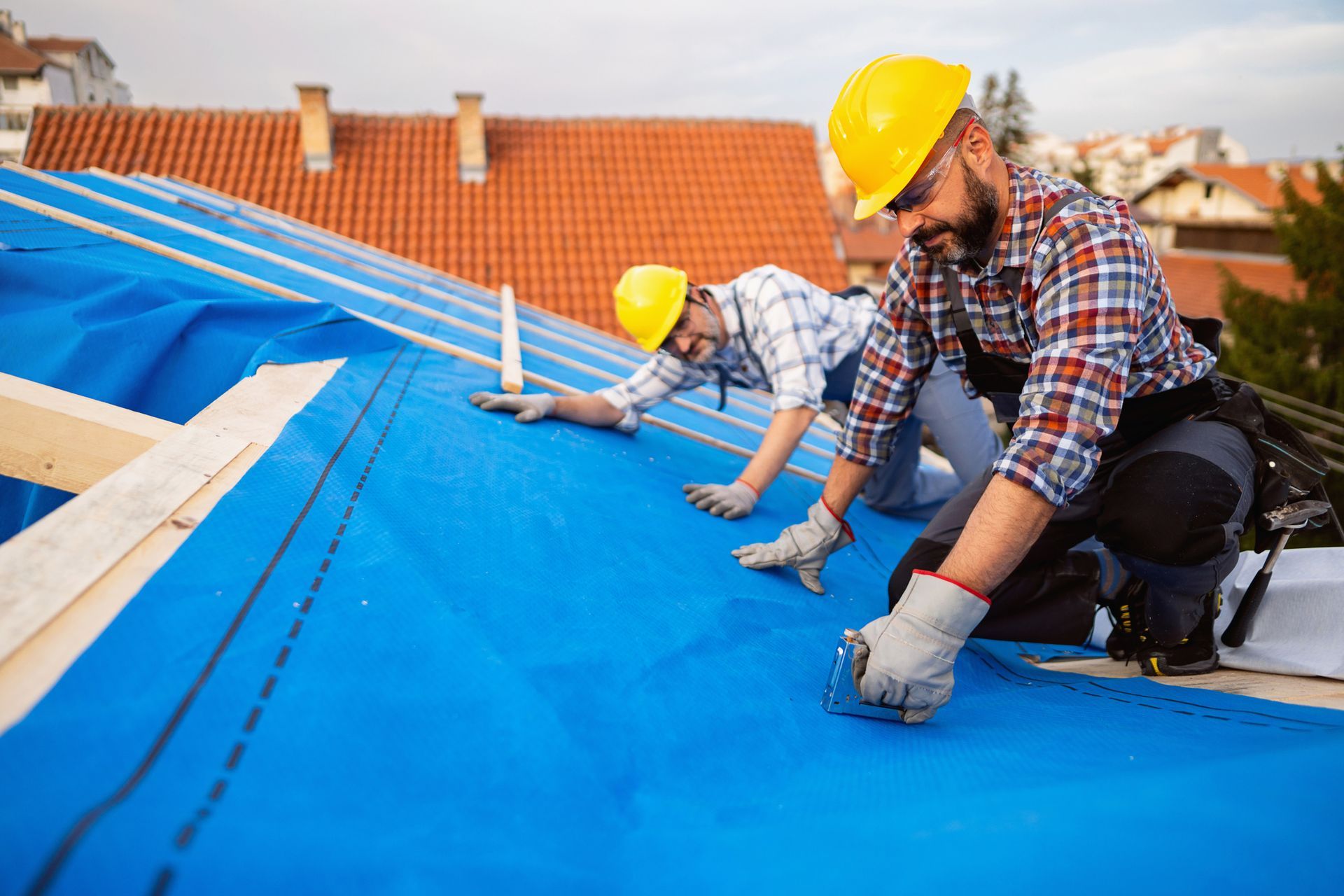Two mid-adult male residential roofing contractors, placing an vapor permeable foil for an roof. 
