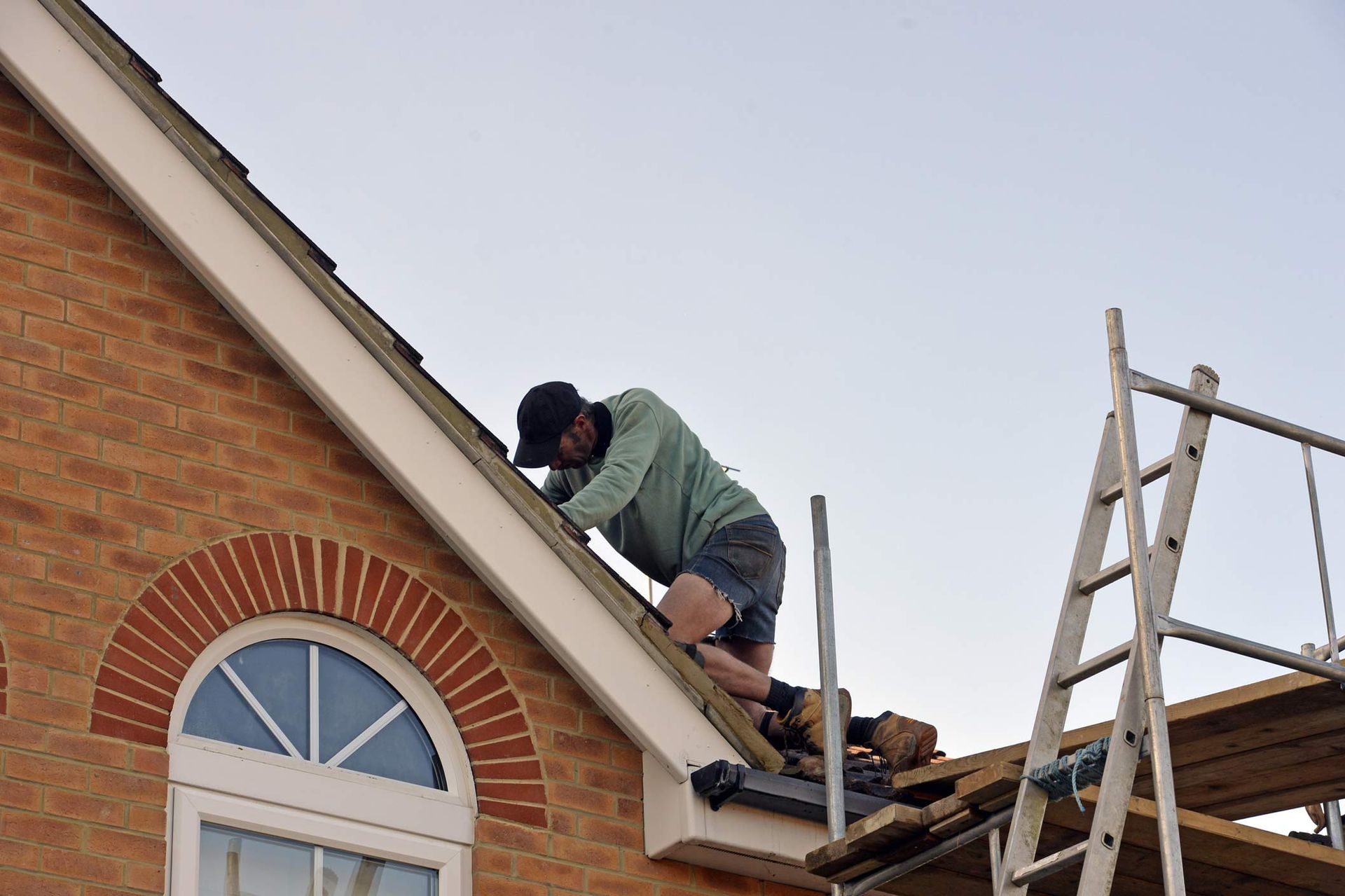 Residential roofing contractor repairing roof shingles on a brick home with arched window. Residential roofing contractor repairing roof shingles on a brick home with arched window.
