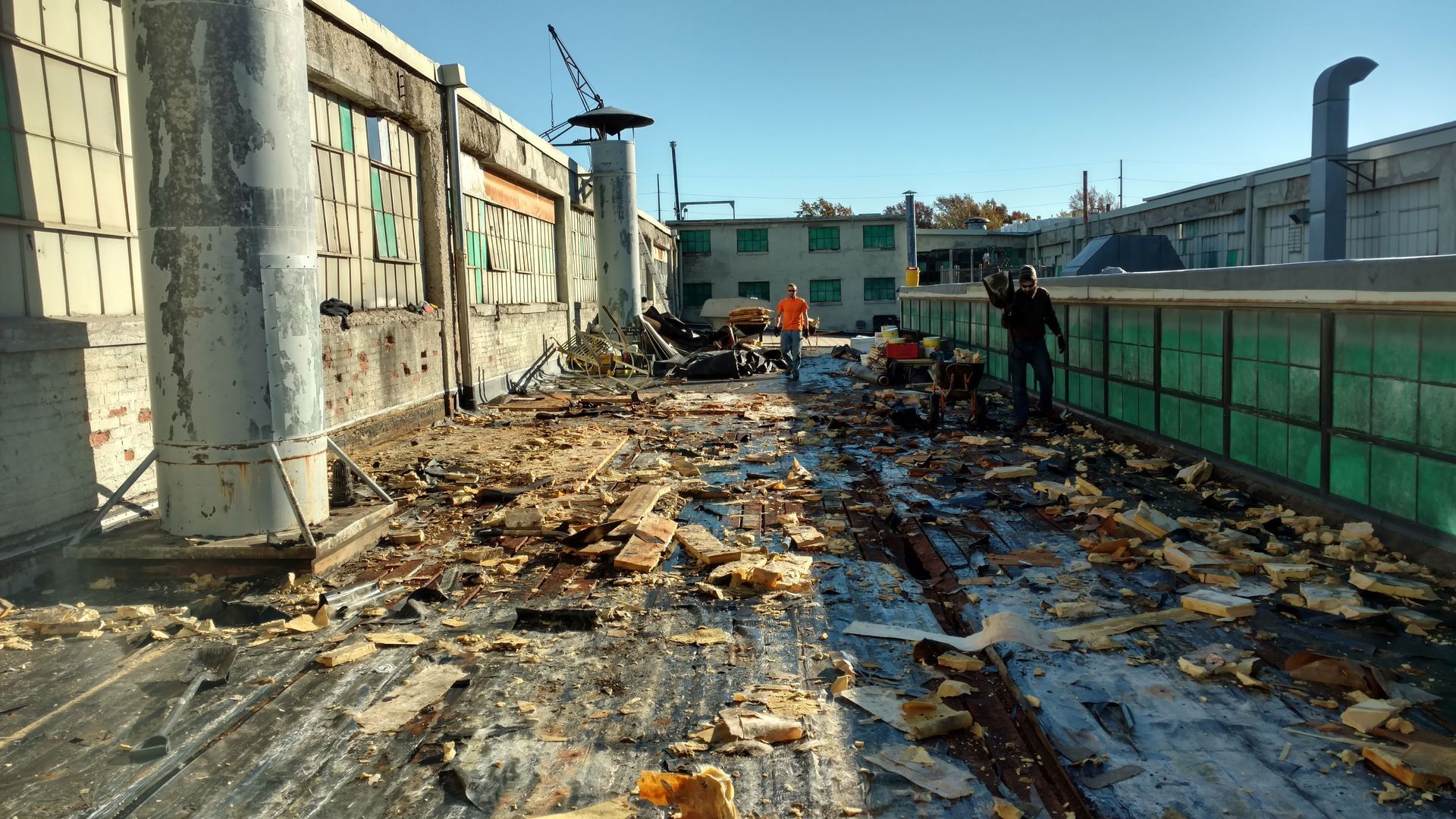 Construction workers survey a roof covered in debris and insulation material at an industrial facility.