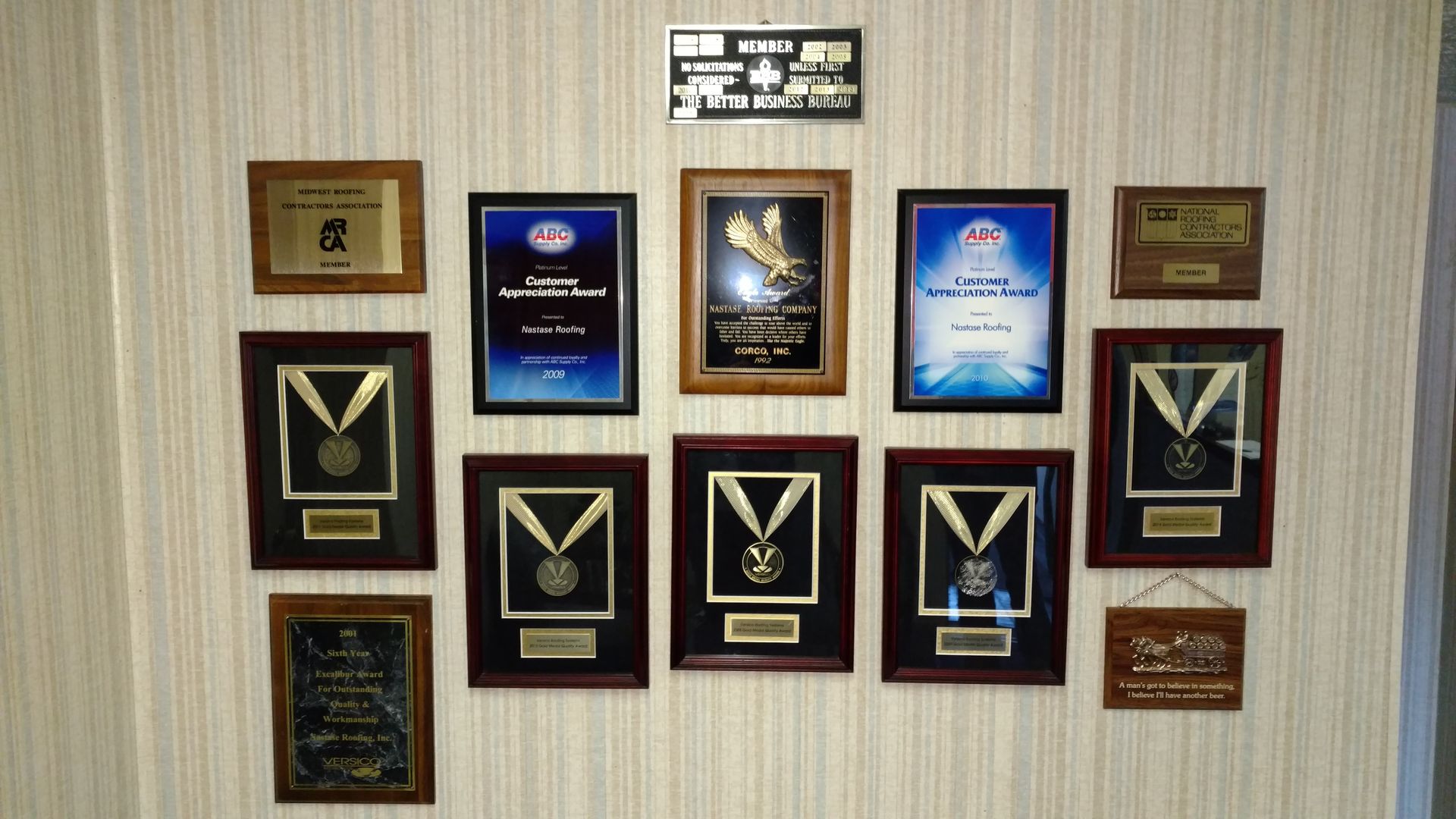 A wall displaying numerous framed award plaques and medals arranged in a gallery style on a striped wallpaper background.