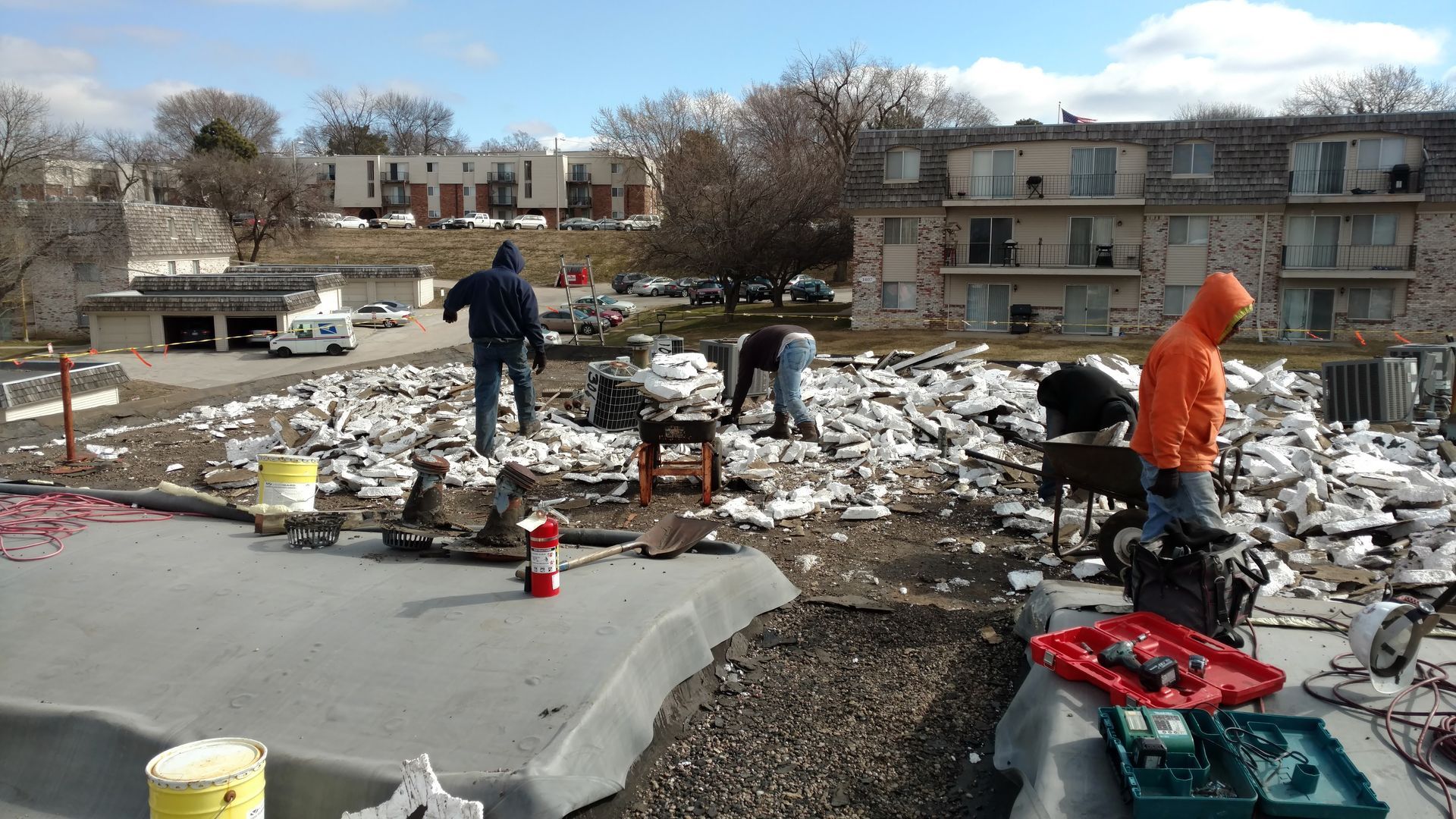 Workers perform roofing repairs on a building, removing debris amidst an ongoing construction project.