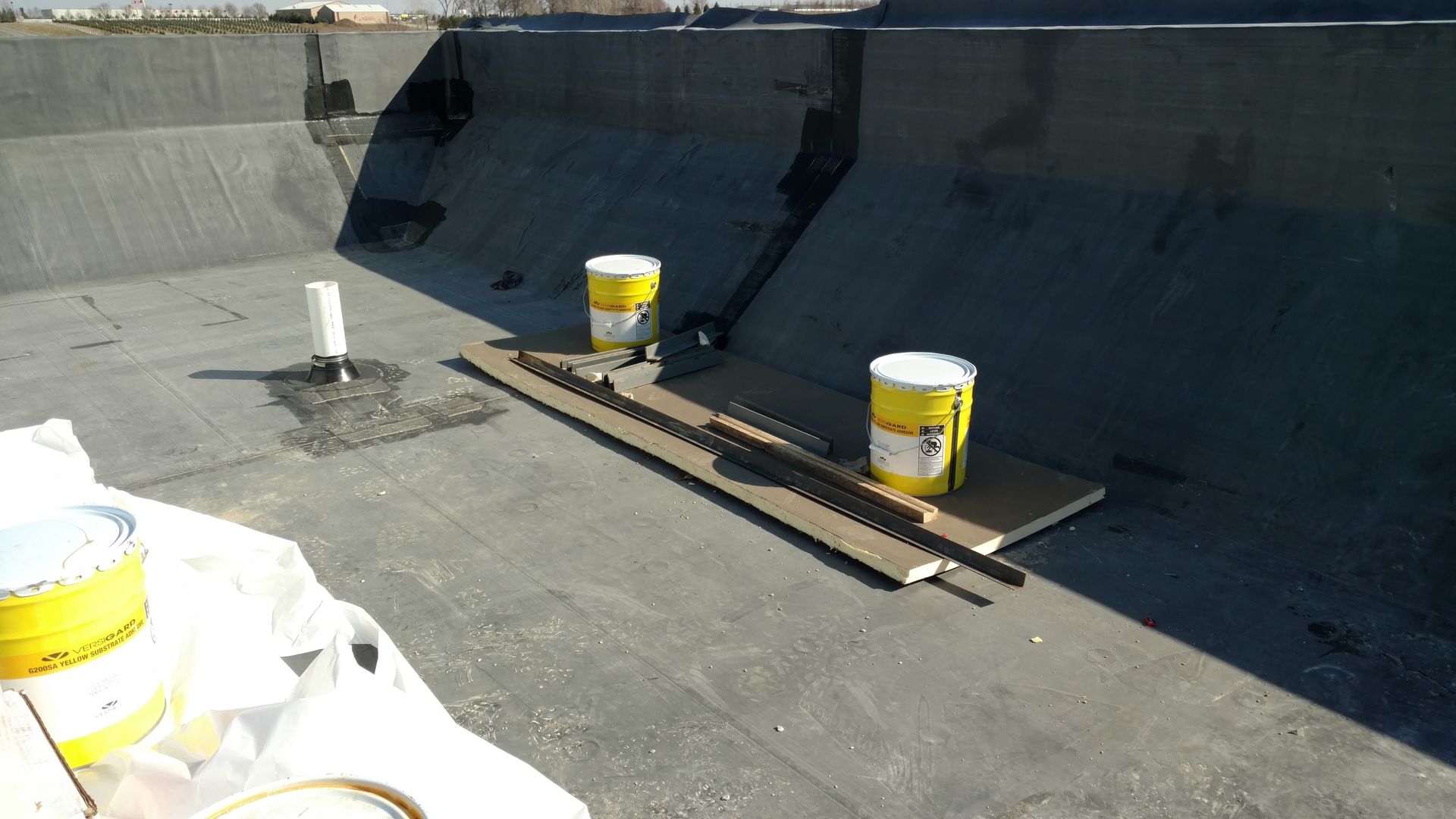 Construction materials, including two yellow buckets and metal strips, sitting on a dark, flat commercial rooftop.