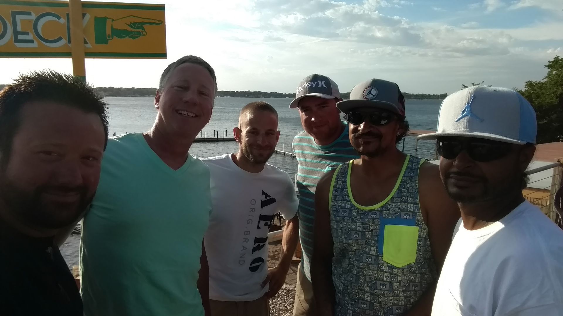 A group of six people posing for a photo outdoors near a body of water with a 