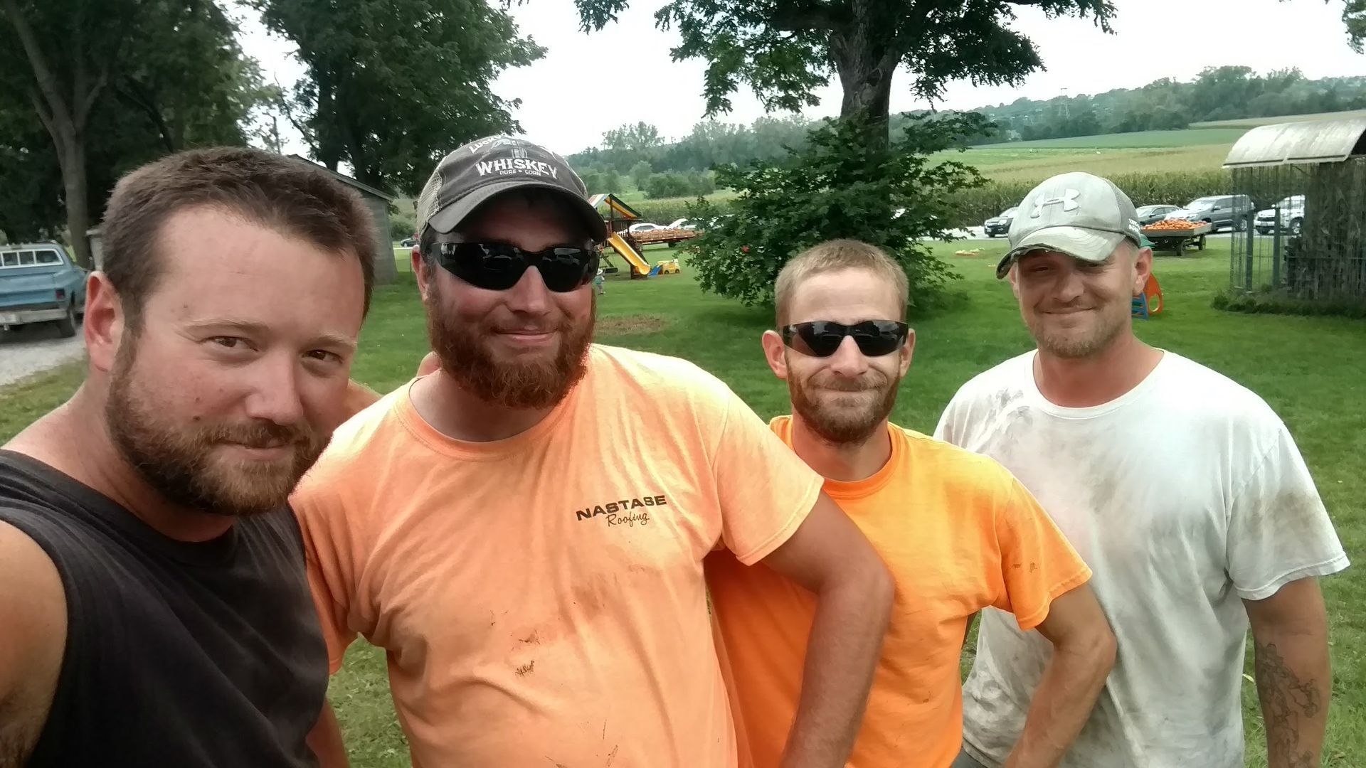 Four men stand outdoors in a grassy field, posing together for a photo.