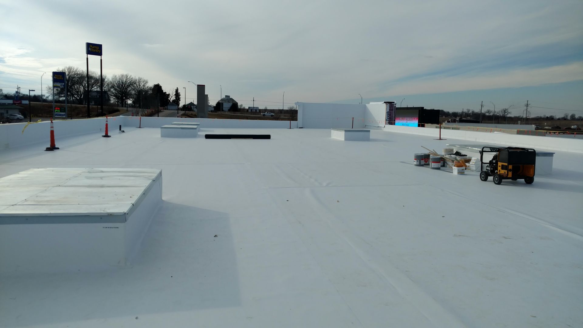 A wide, flat white roof on a sunny day with small HVAC units and construction equipment scattered across the surface.