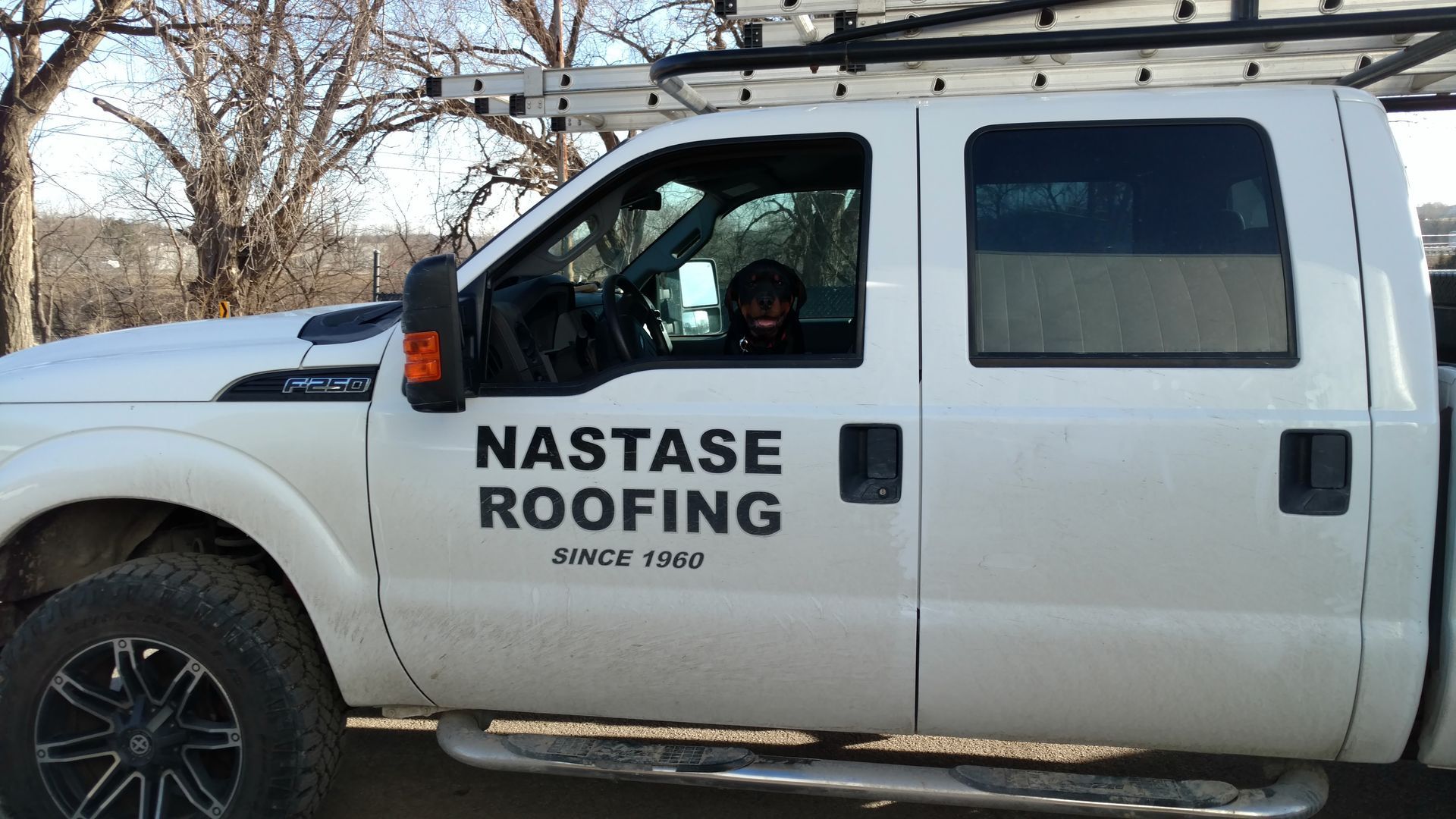 A white Nastase Roofing pickup truck with a roof rack parked outdoors.