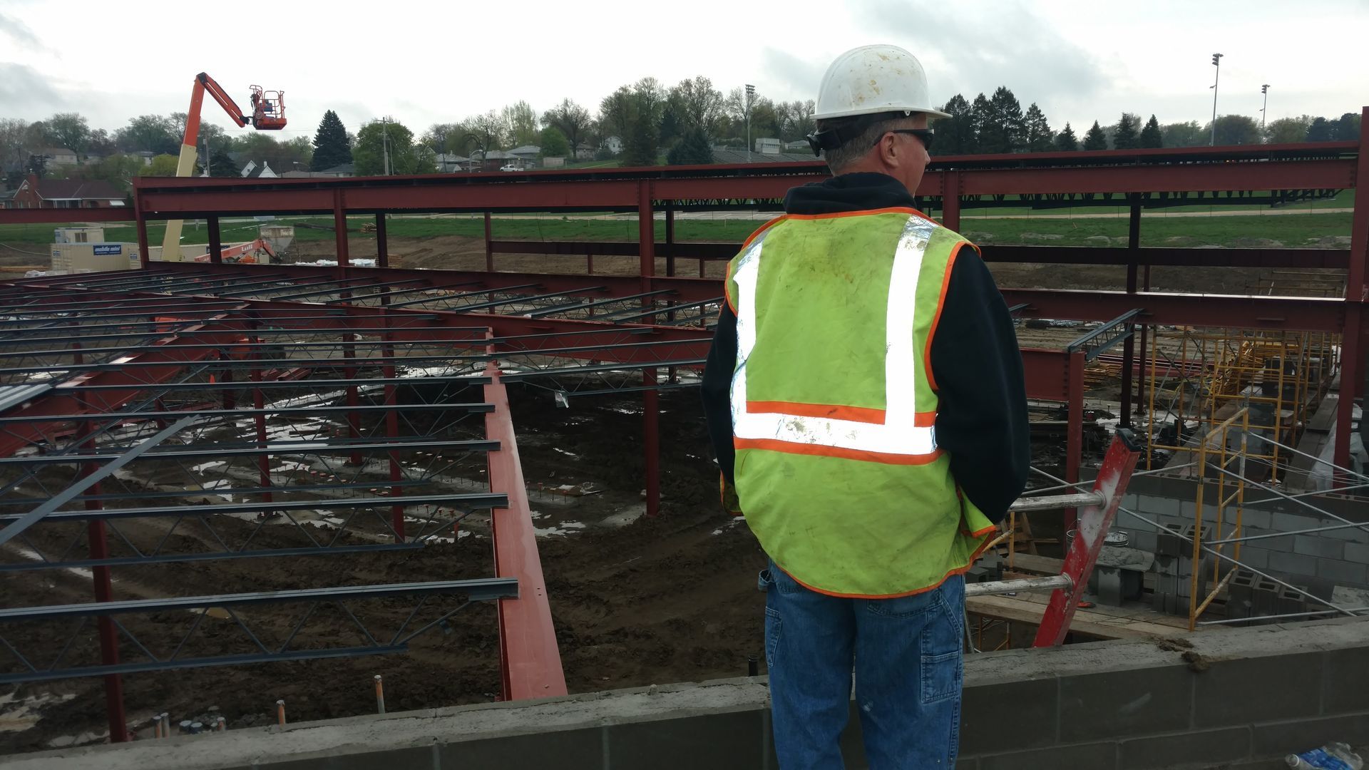 A worker in a hard hat and high-visibility vest overlooks a construction site with exposed steel framing.
