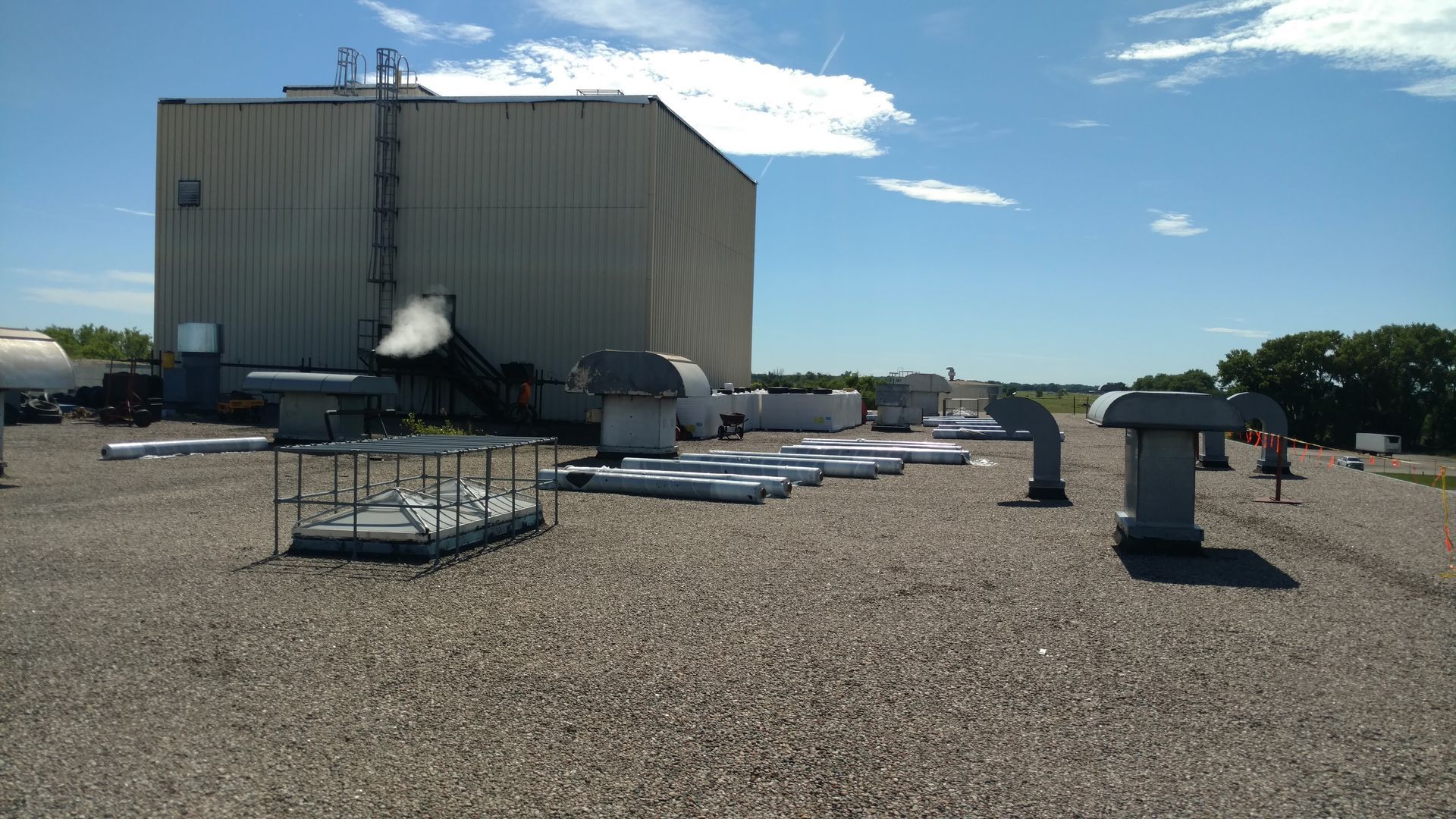 A large industrial building with roof vents and gravel surfacing under a blue sky.
