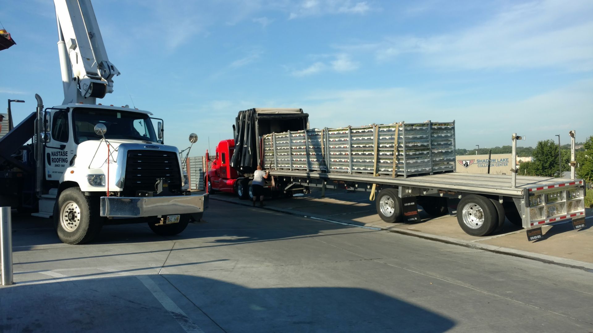 A white utility truck and a red semi-truck with a flatbed trailer loaded with metal scaffolding on a sunny road.