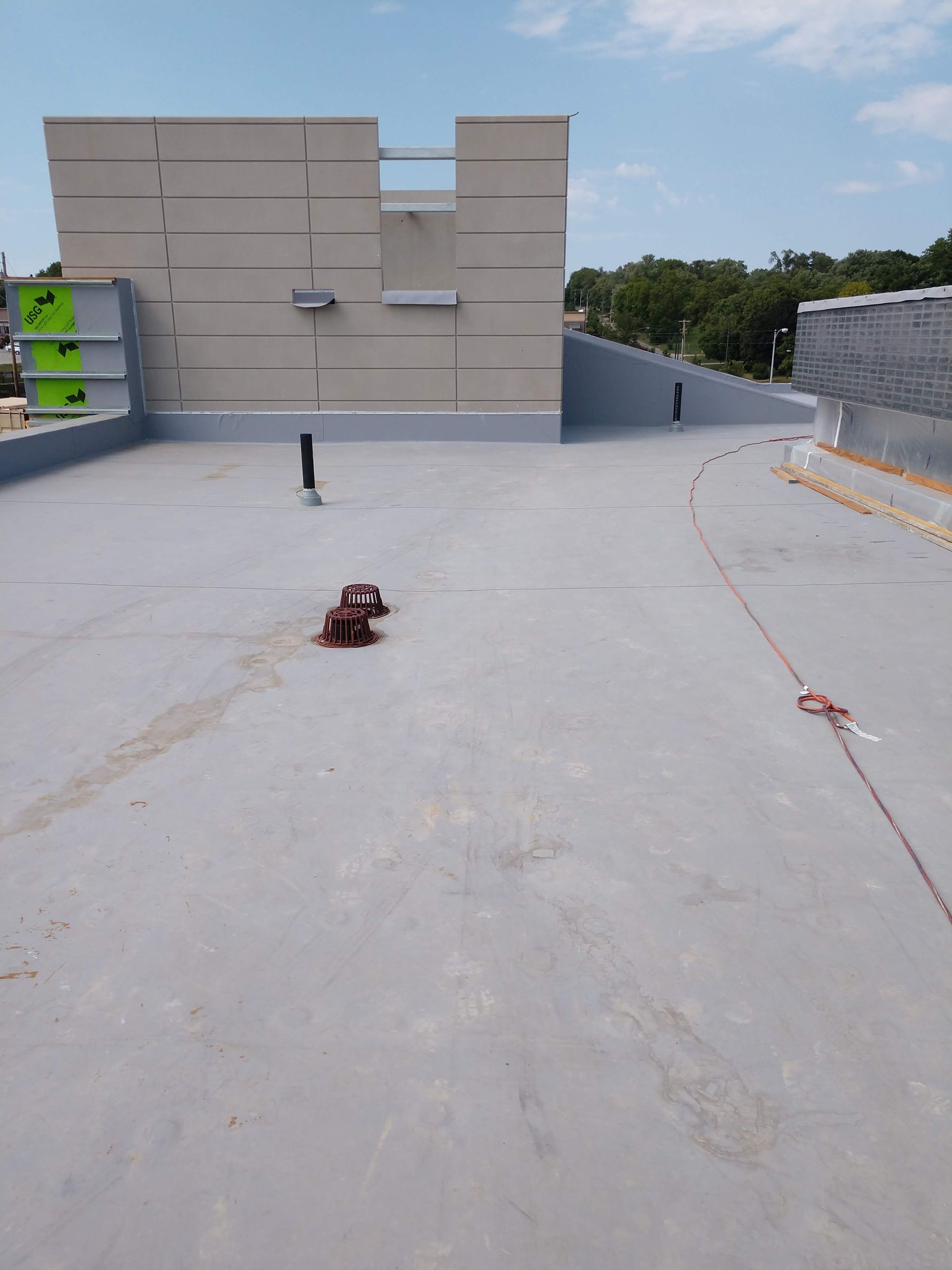 A view of a flat, light grey industrial rooftop under a blue sky, featuring mechanical equipment and a beige wall.