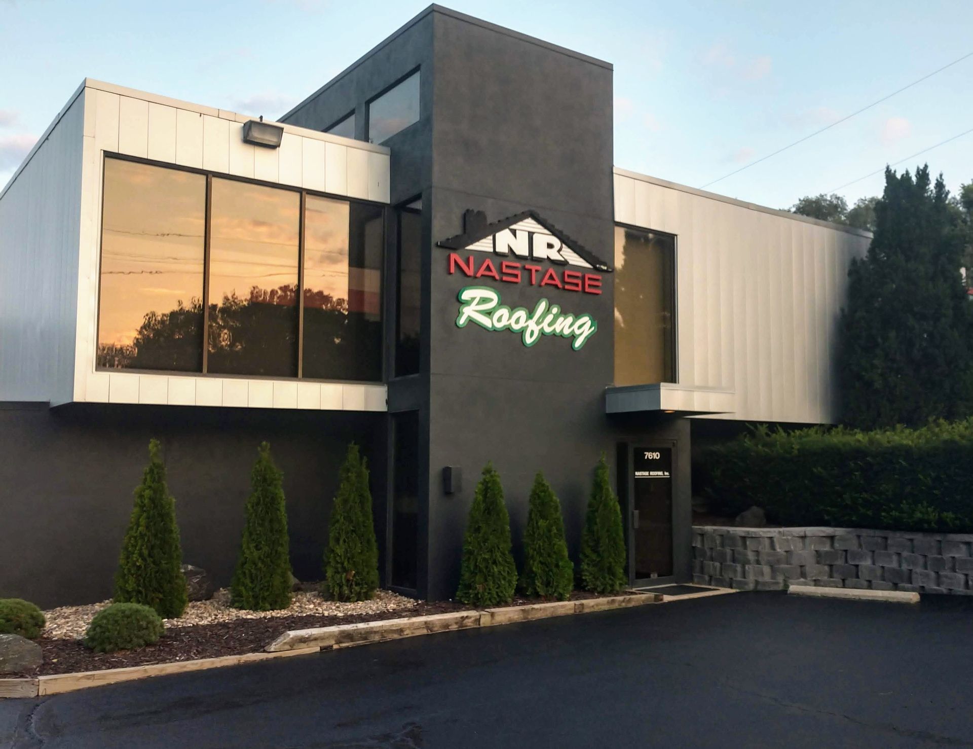 A modern commercial building with a black center tower displaying the Nastage Roofing logo, flanked by tinted windows.