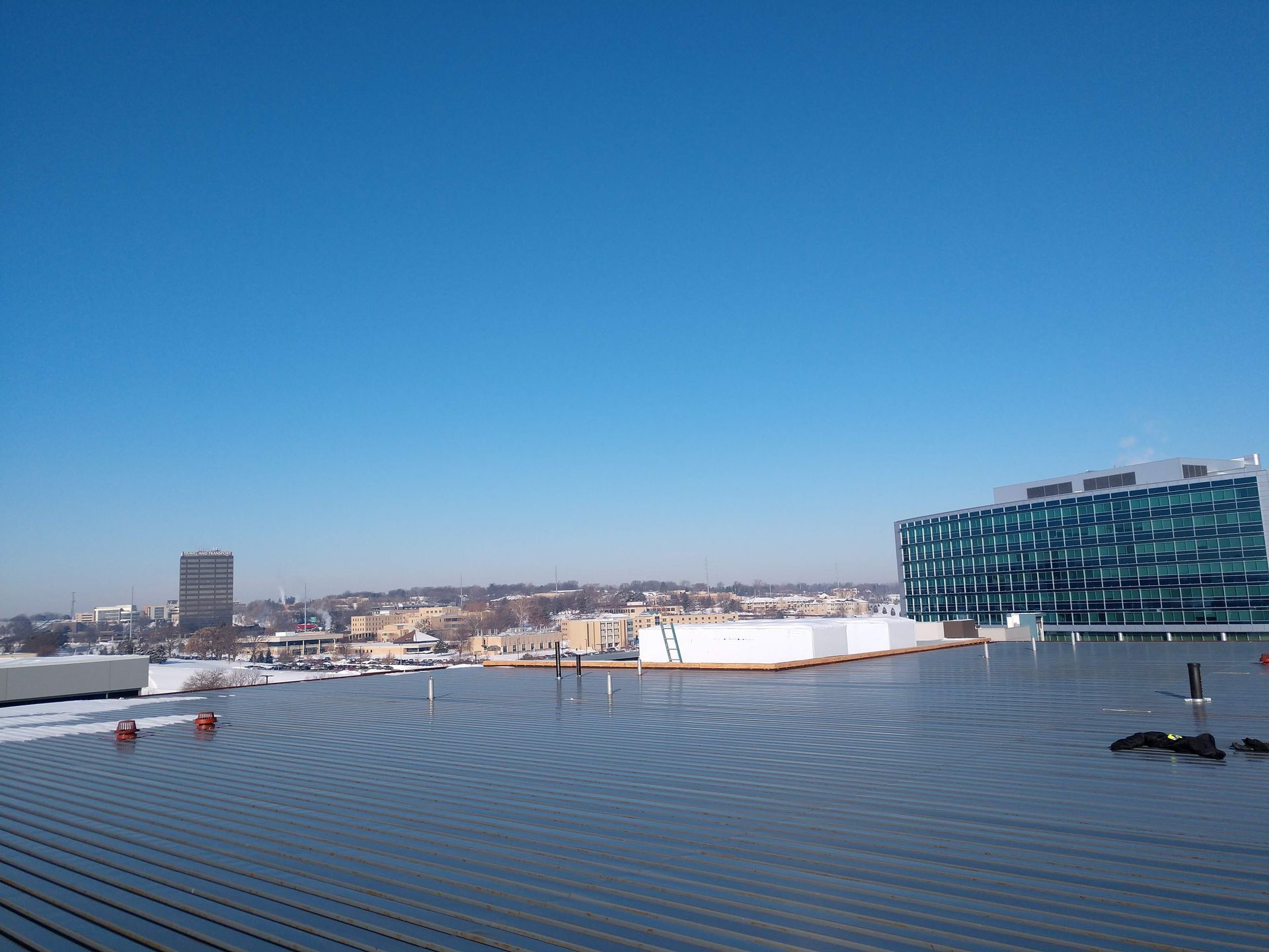 A clear blue sky overlooks a flat, dark roof in the foreground with city buildings in the distance.