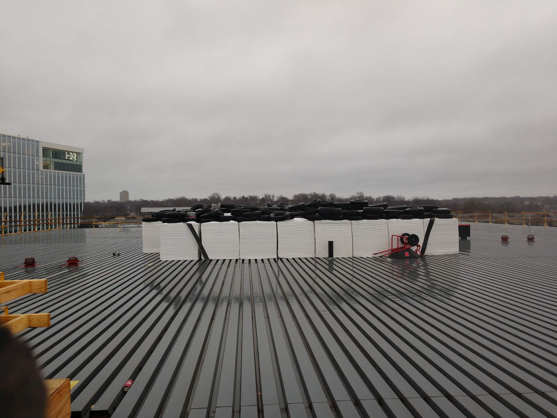 Stacked white pallets topped with black bags sit on a dark, circular grooved rooftop under a cloudy sky.