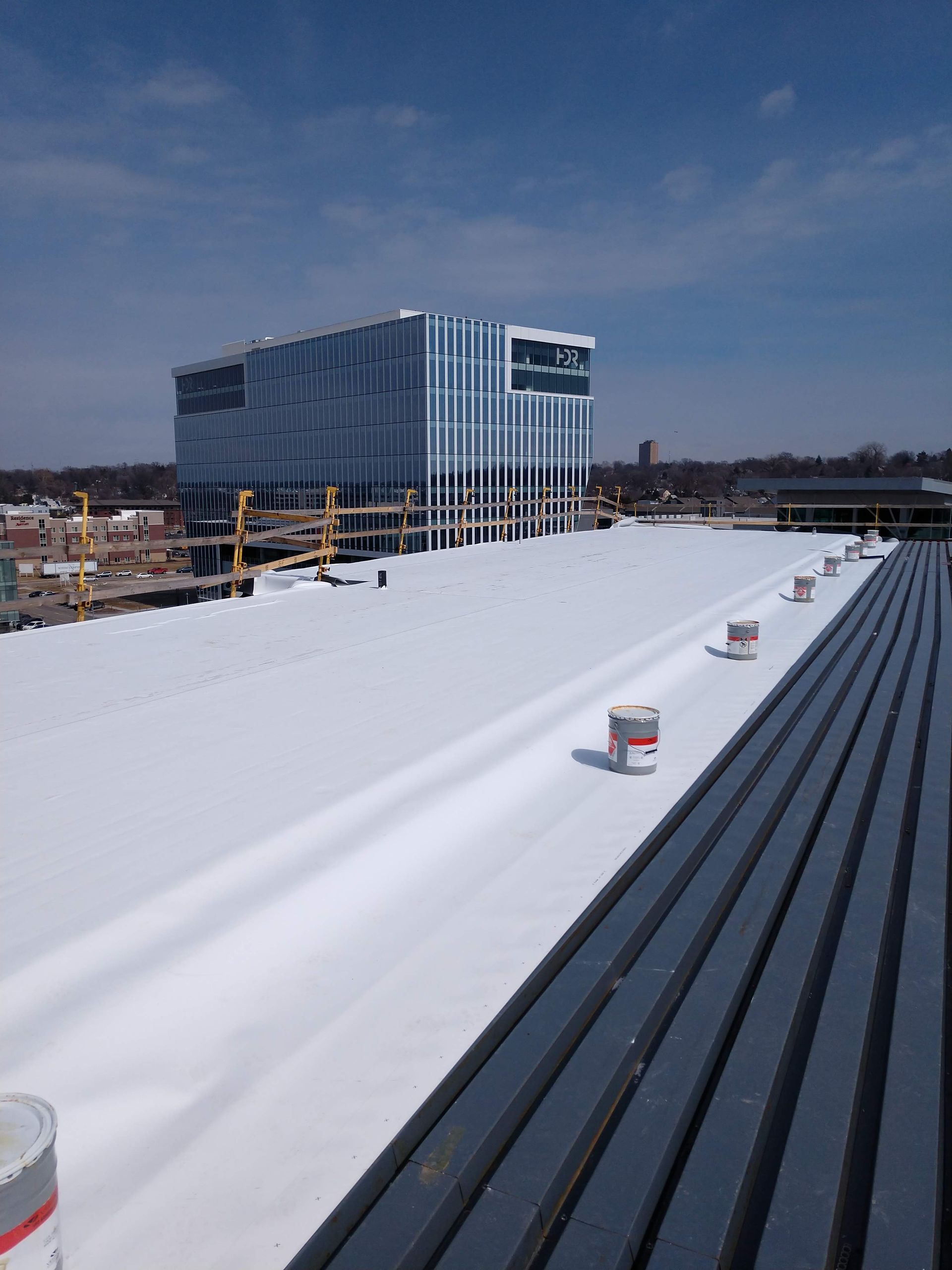 A view from a rooftop looking out at a modern glass building under a clear blue sky, with a white roof surface below.