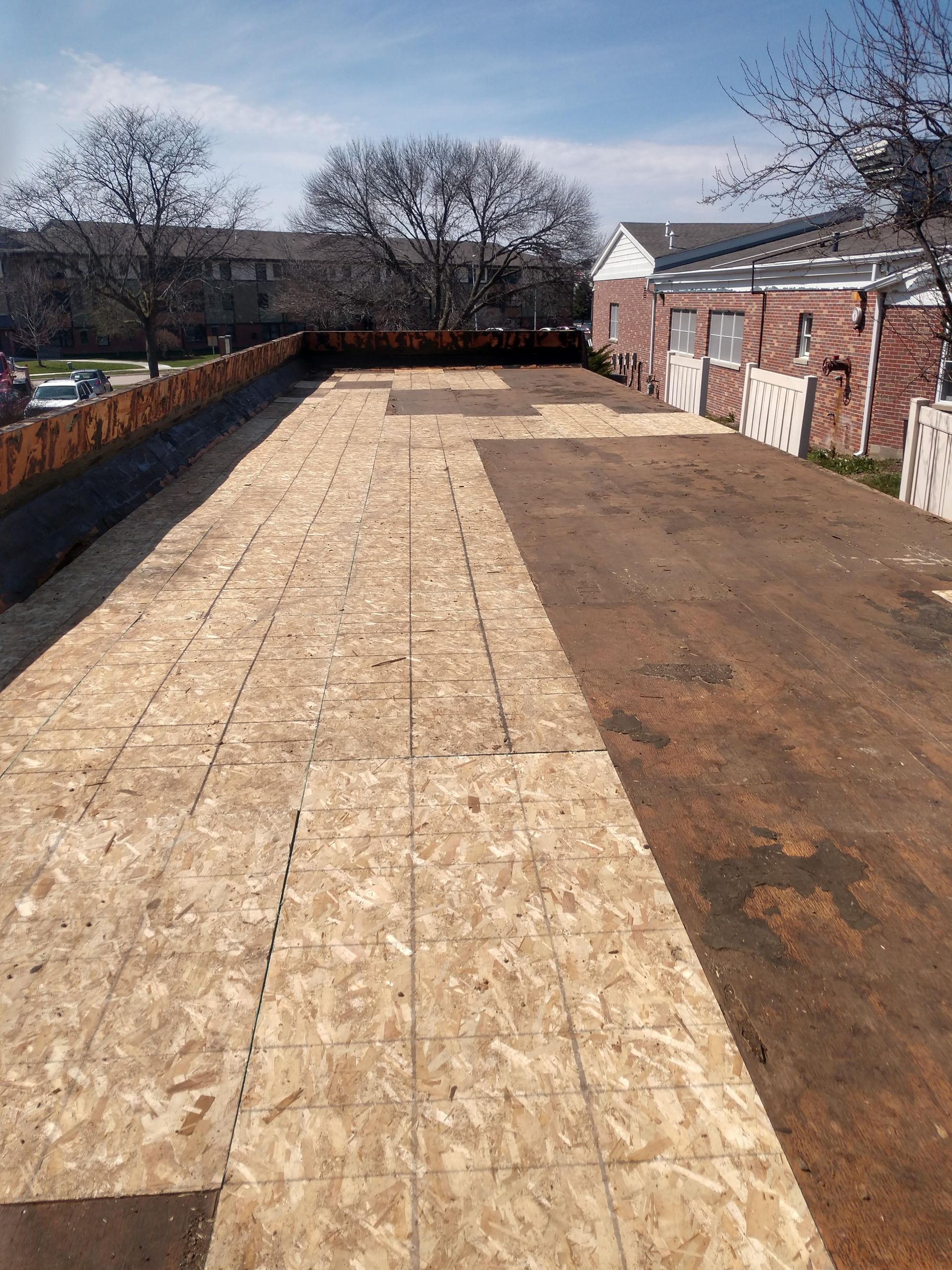 A flat roof under construction, showing a mix of newly installed plywood decking and exposed underlayment.