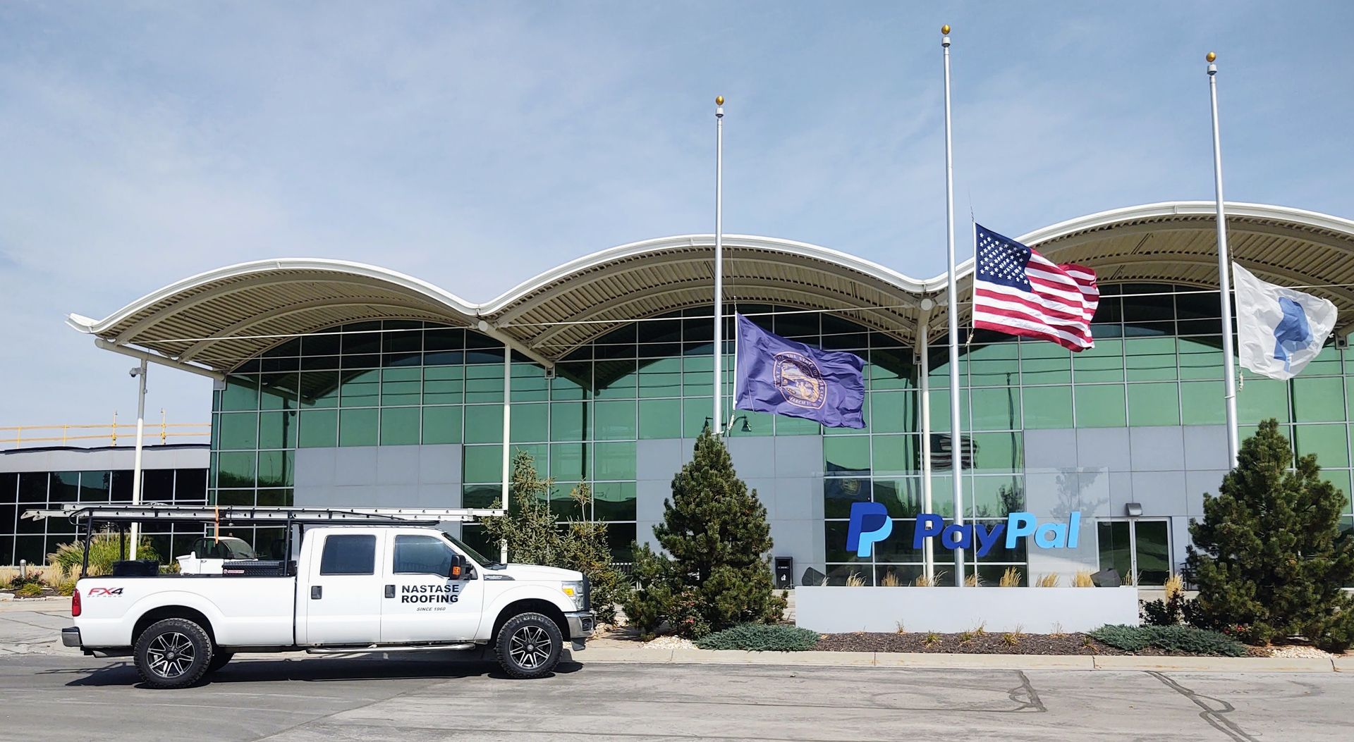 A white pickup truck parked in front of a modern glass building with a PayPal sign and flags flying at half-mast.