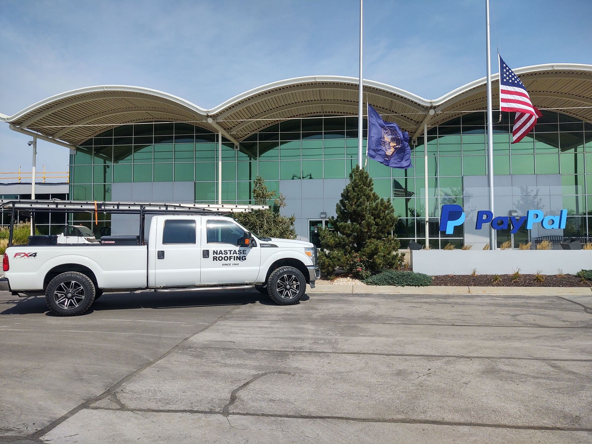 A white work truck parked in front of a modern glass building with a PayPal sign and flags flying out front.