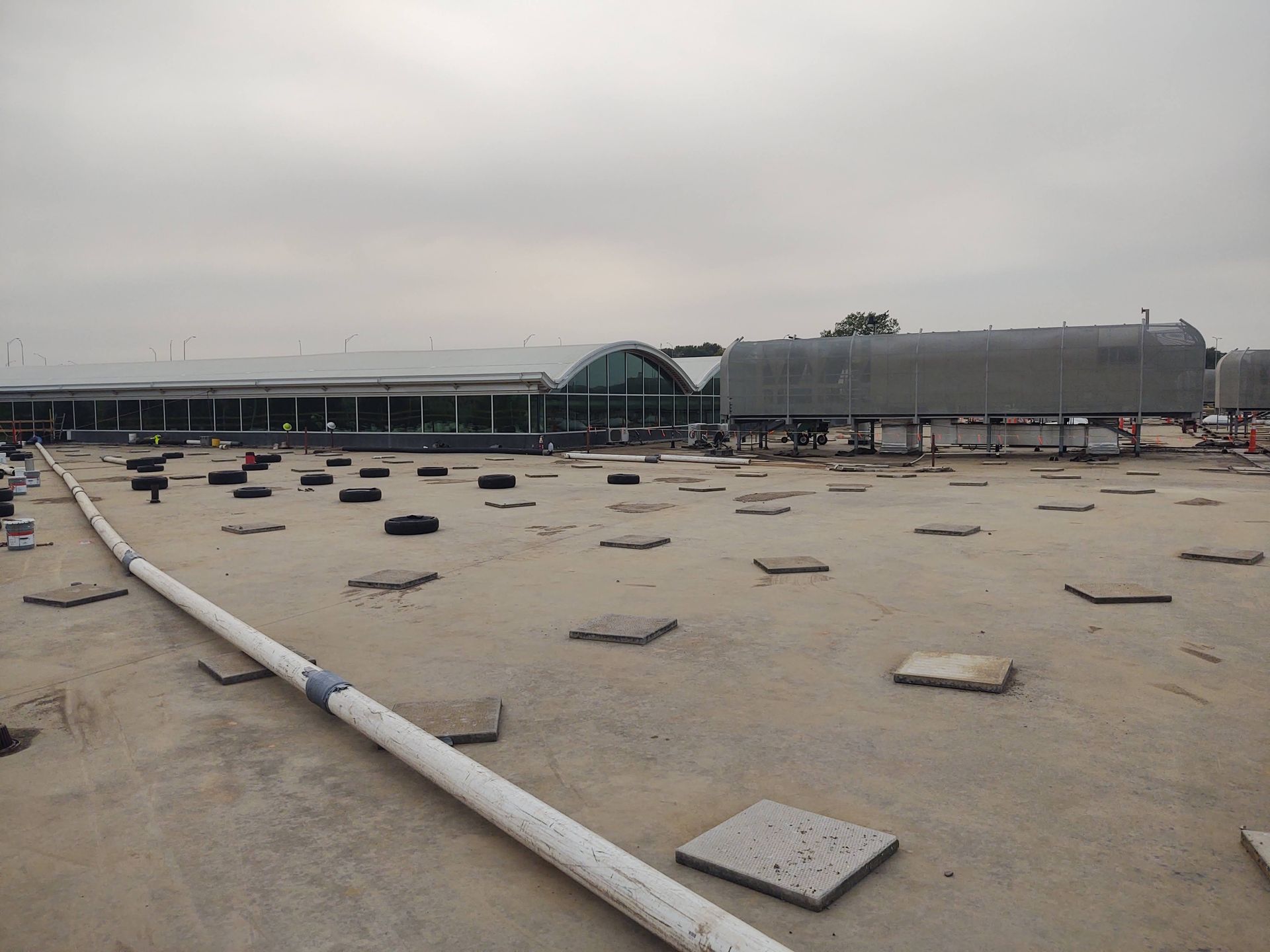 A wide, flat roof with scattered square concrete pavers and a long pipe, leading toward a modern curved terminal building.